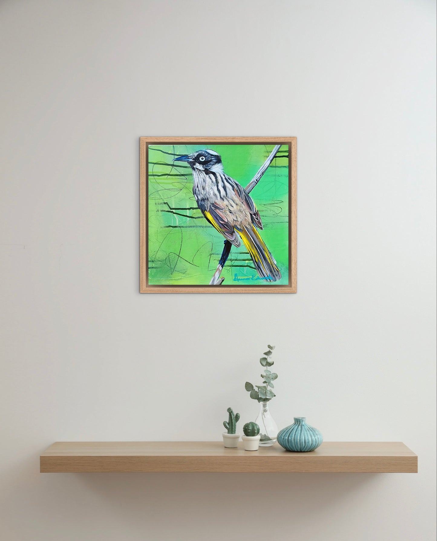 Framed artwork of a bird on a white wall above a wooden shelf with decorative items.