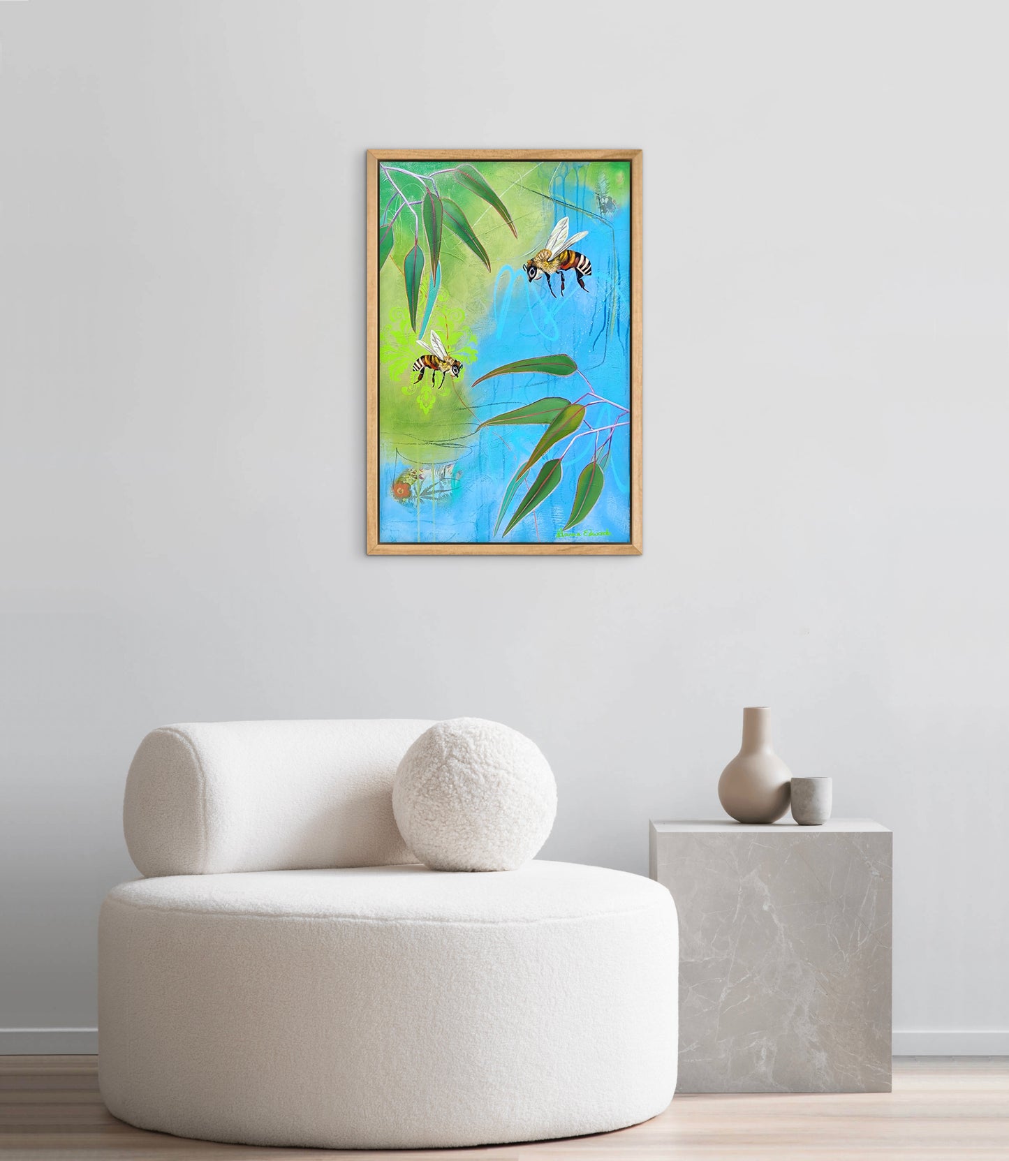 Framed artwork of bees and leaves on a wall above a white armchair.