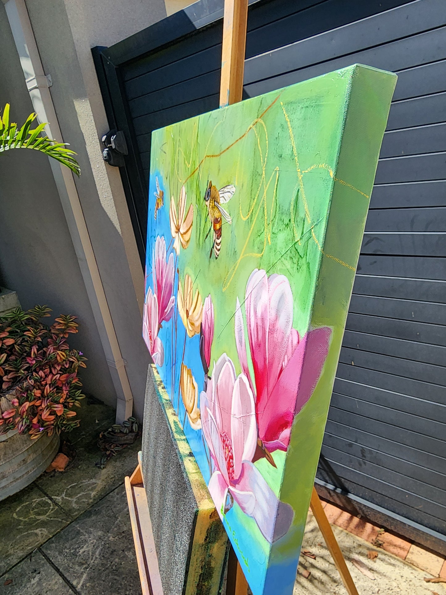Colorful painting side view of flowers and bees on a wooden easel outdoors.
