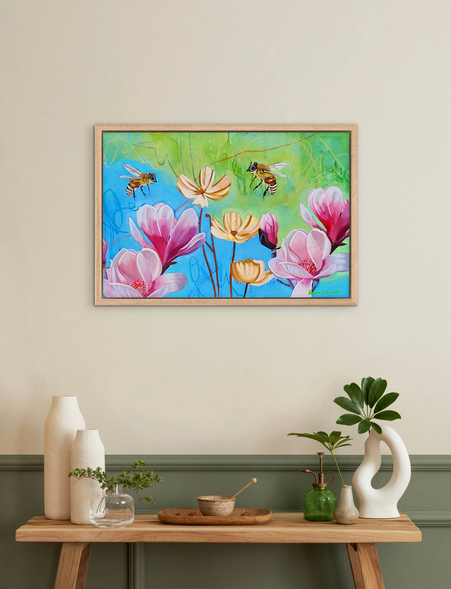 Framed artwork of flowers and bees on a wall above a wooden table with decorative items.