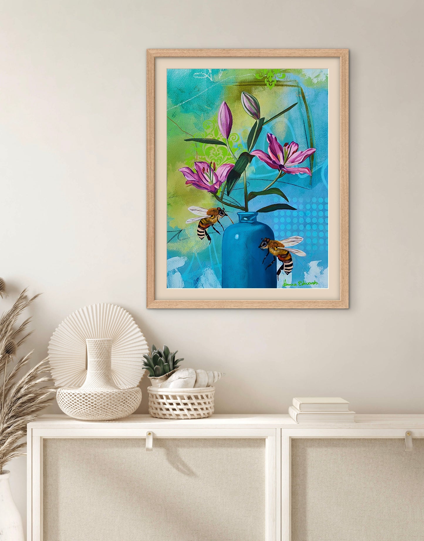 Framed artwork of flowers and bees on a wall above a white cabinet with decorative items.