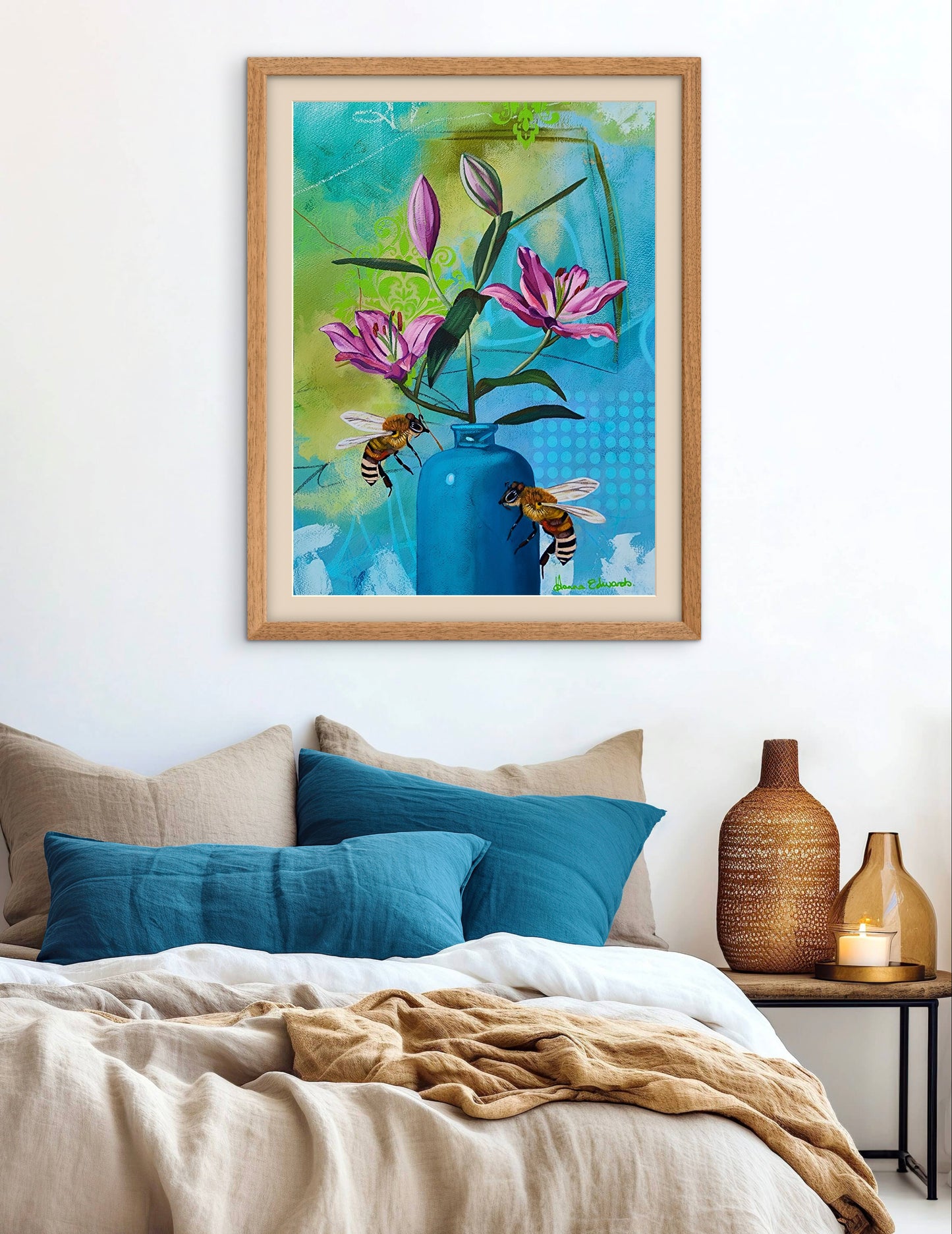 Framed artwork of flowers and bees on a wall above a bed with decorative pillows and vases.