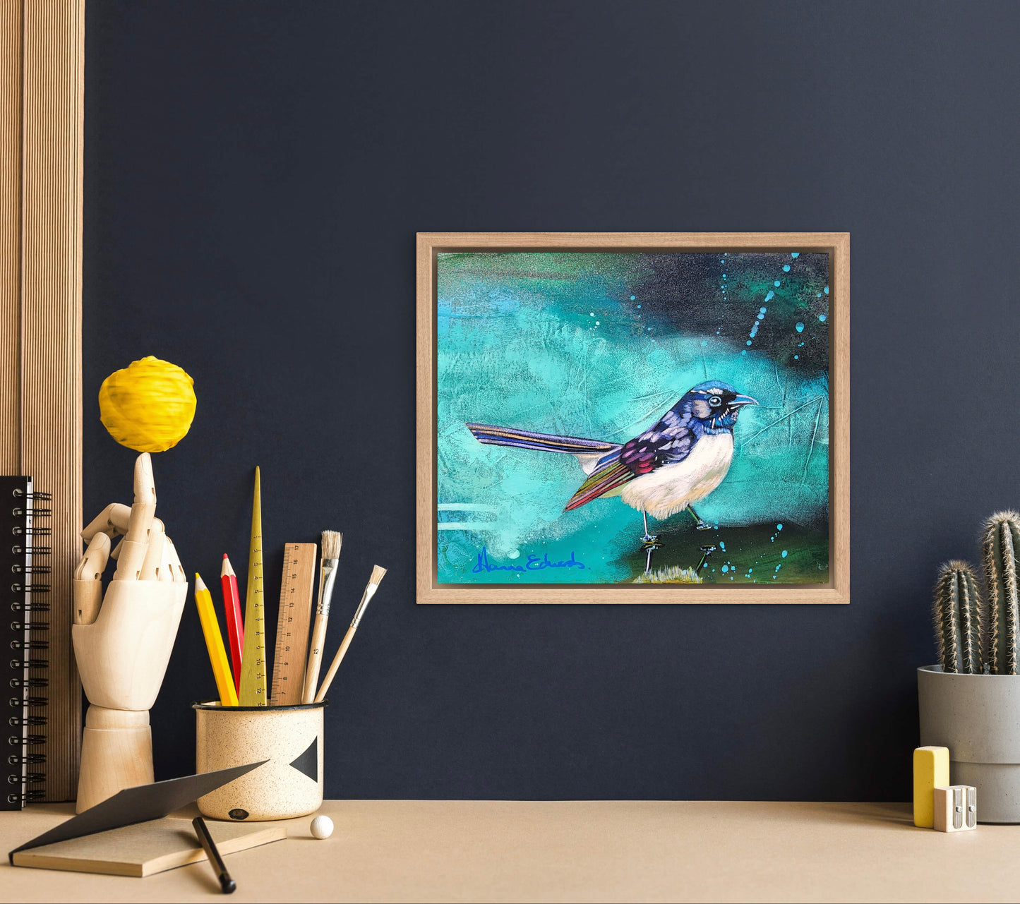 Framed artwork of a bird on a dark blue wall with office supplies below.