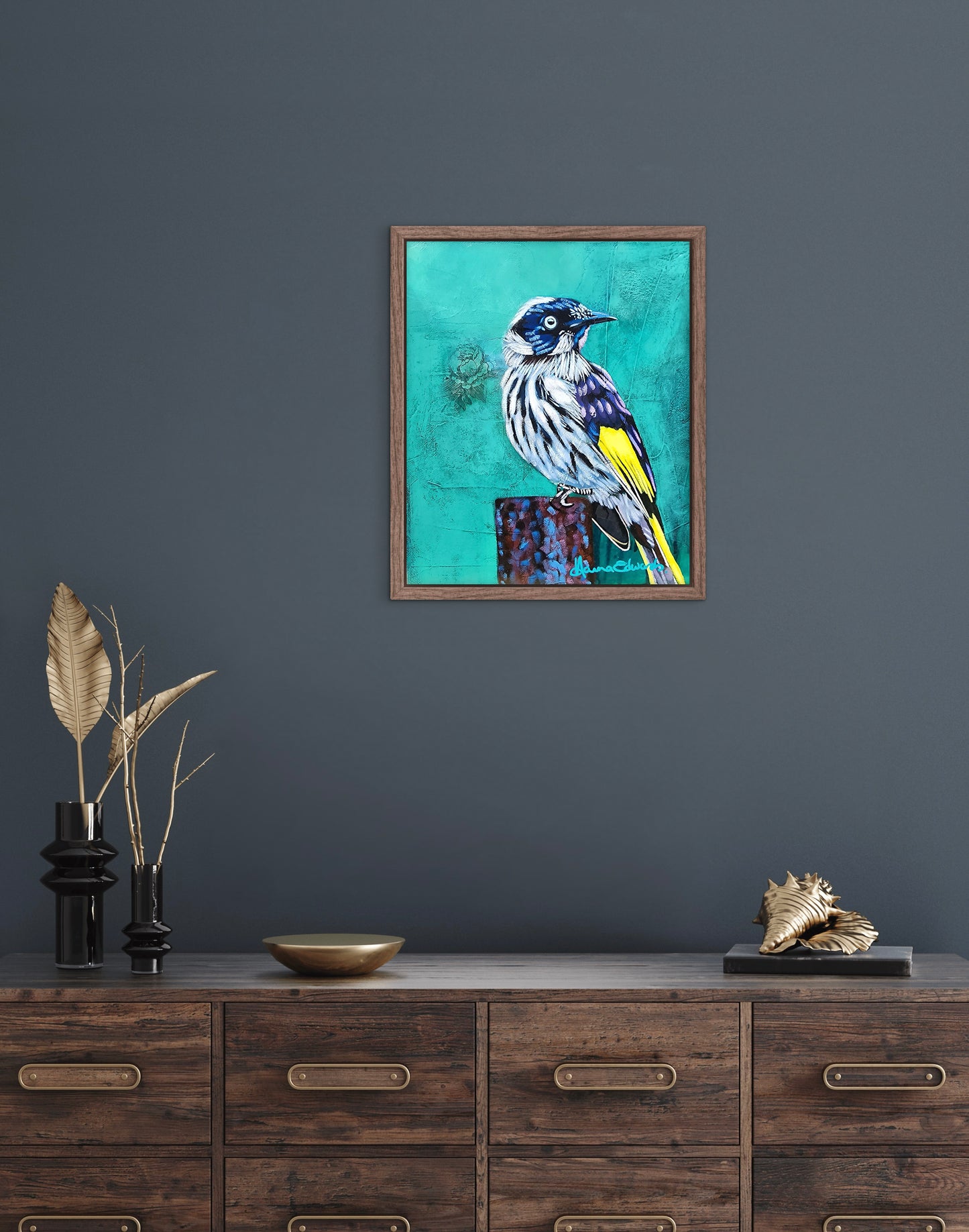 Framed artwork of a bird on a teal background above a wooden cabinet.