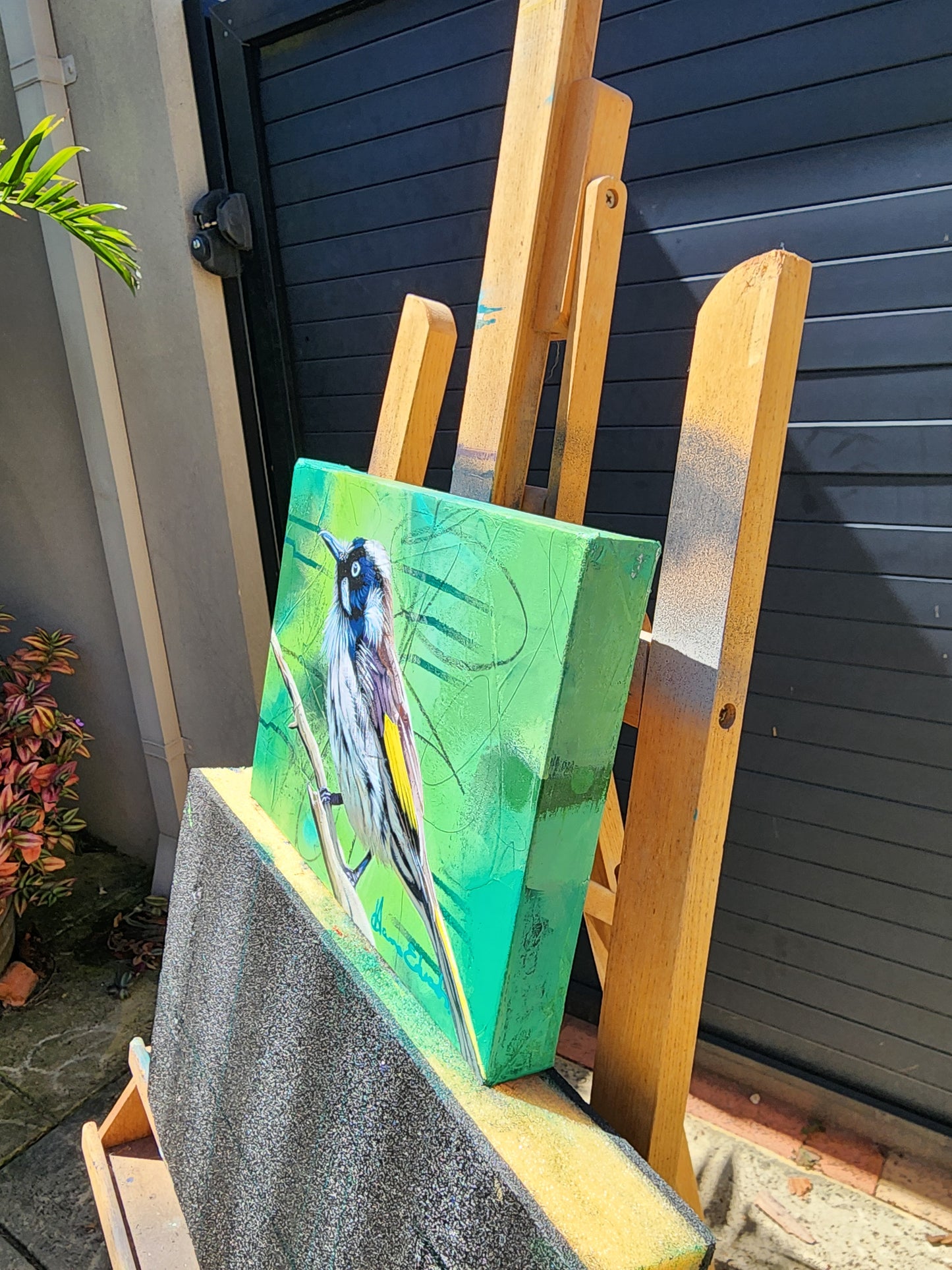 Wooden easle with a green painting of a bird side view