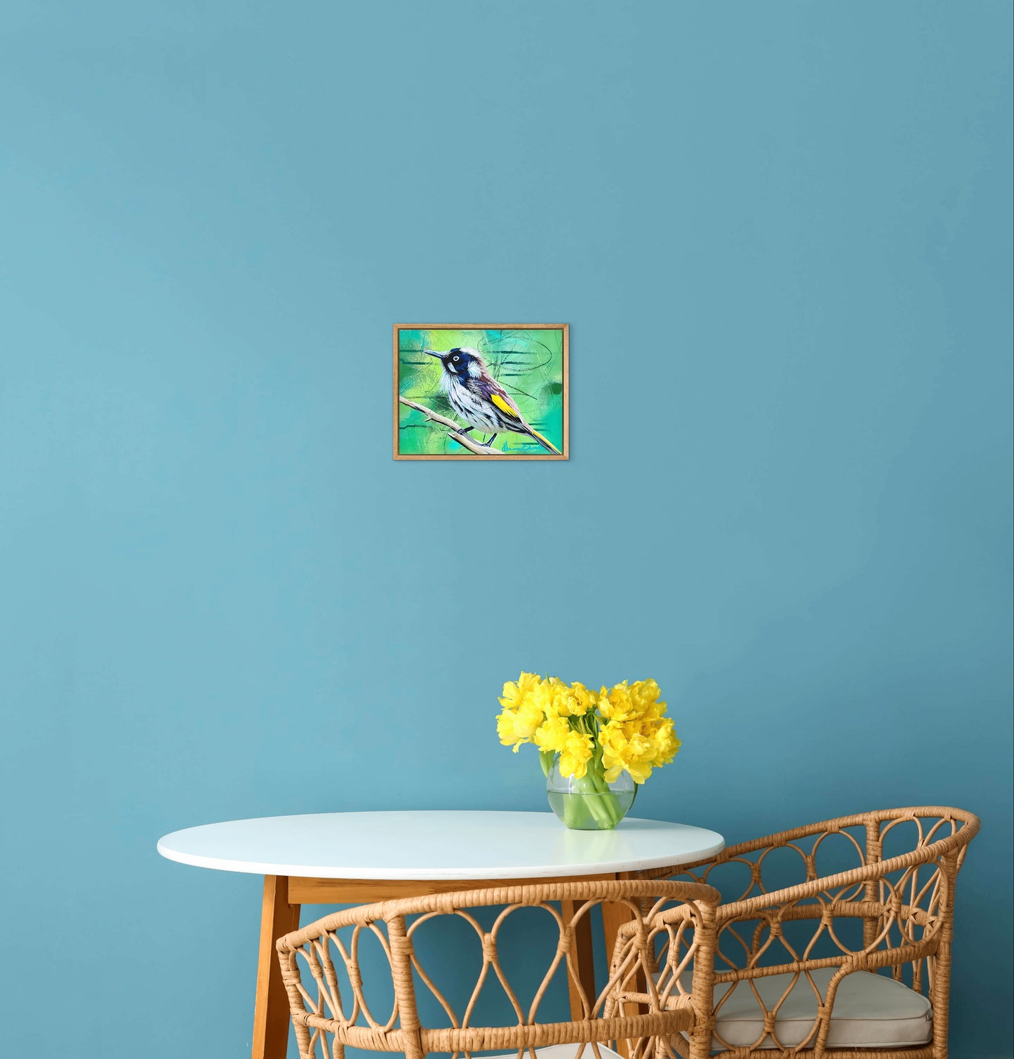 Framed painting of a bird on a blue wall above a table with yellow flowers and wicker chairs.