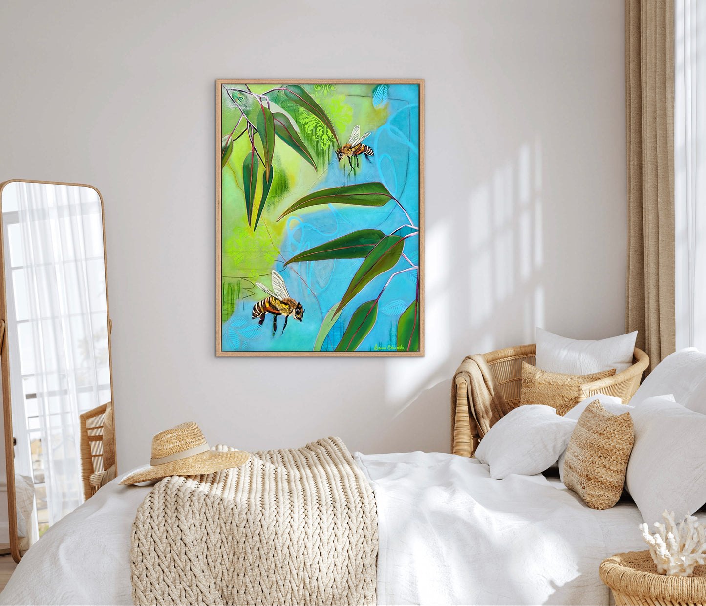 Framed artwork of bees and leaves on a wall above a bed with decorative pillows and baskets.