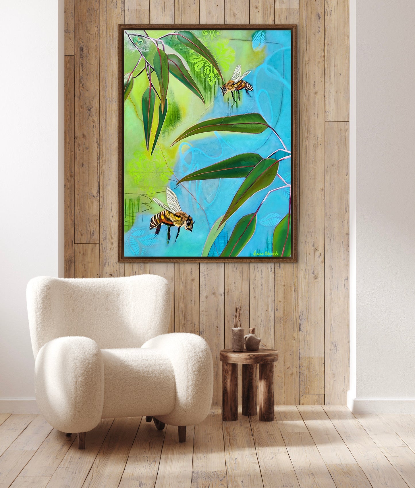 Framed artwork of bees and leaves on a wooden wall above a white armchair.
