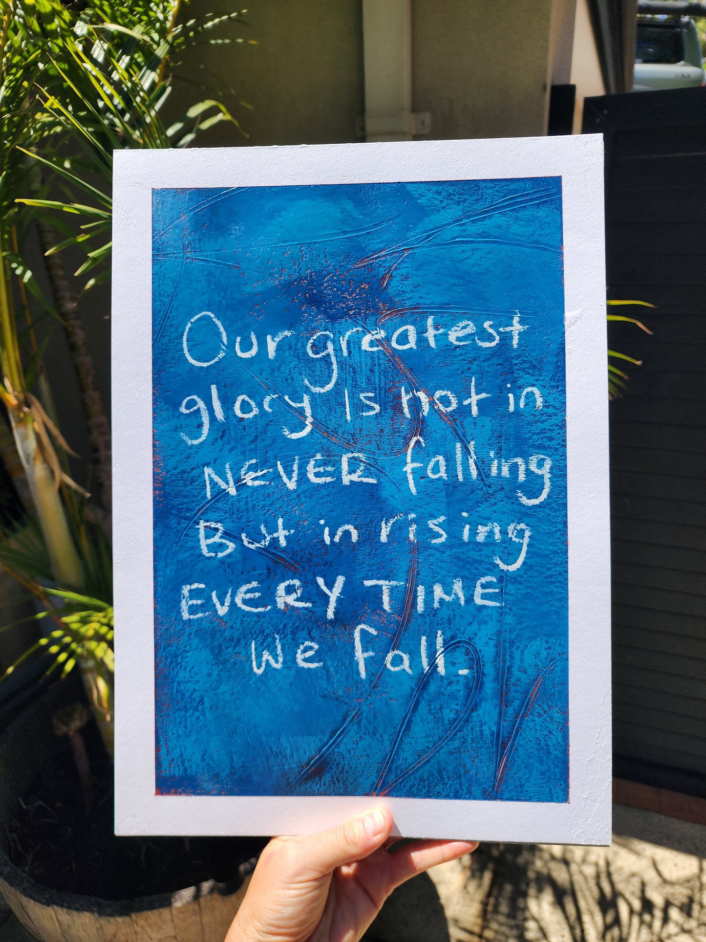 Blue artwork with motivational quote on a blue background, held outdoors.