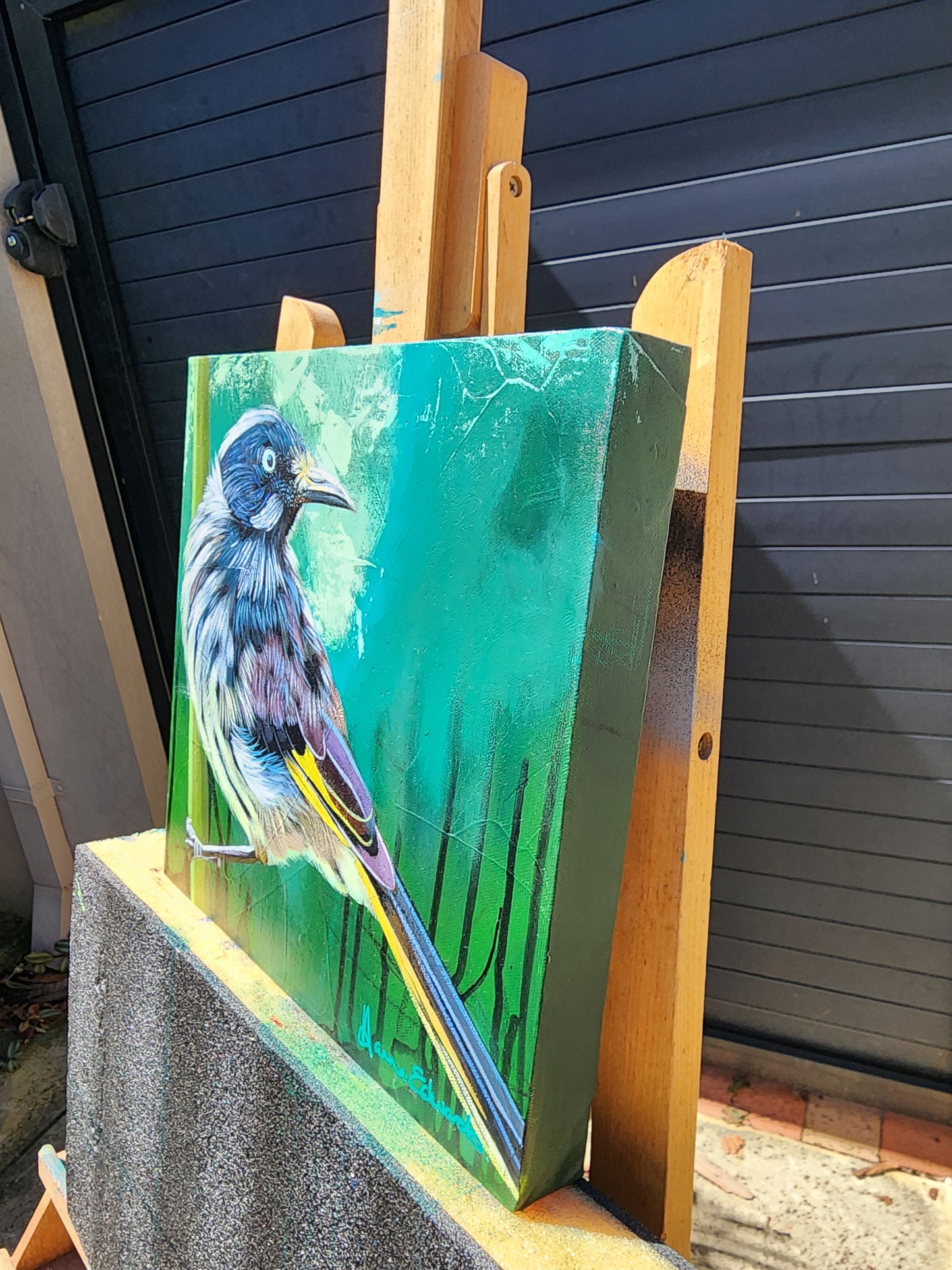 Painting of a bird on a green background side view displayed on an easel.