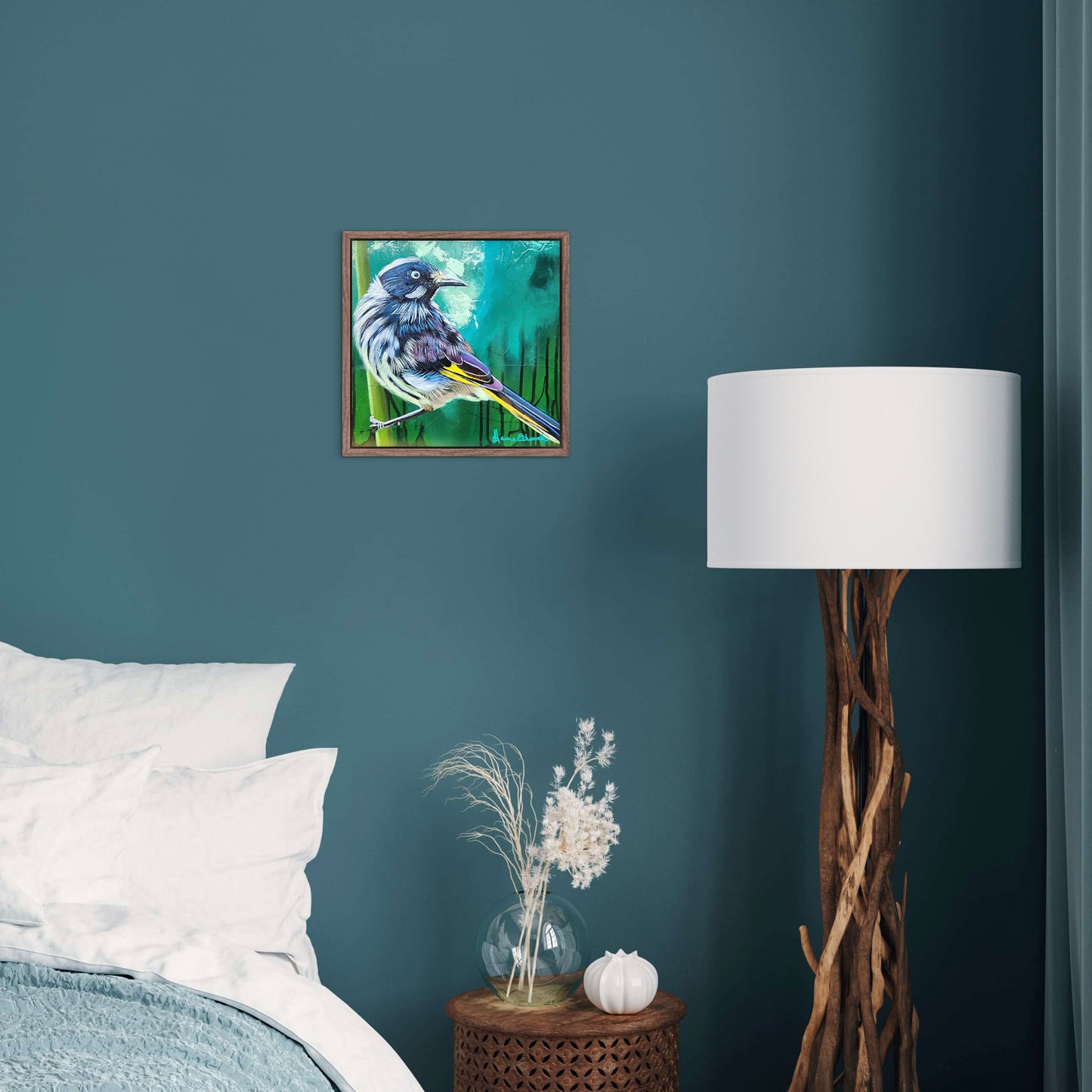 Framed artwork of a bird on a blue wall above a bed with a lamp and decorative items.