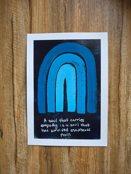 A blue painting with pops of yellow undernesth with a white border featuring a blue and black textured rainbow design and a handwritten quote, "A soul that carries empathy is a soul that has survived enormous pain"