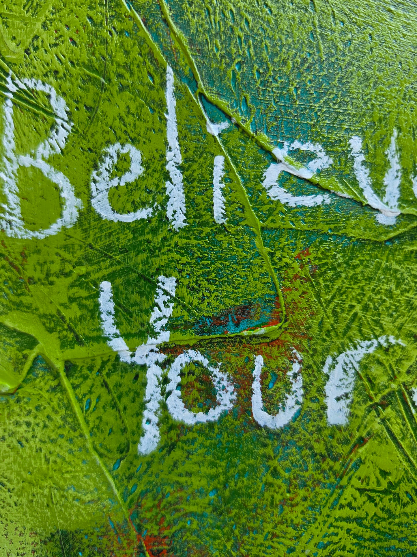 Abstract painting close up in green with green and red pops of colour in underneath layers with words Believe in yourself in white handwriting and texture 