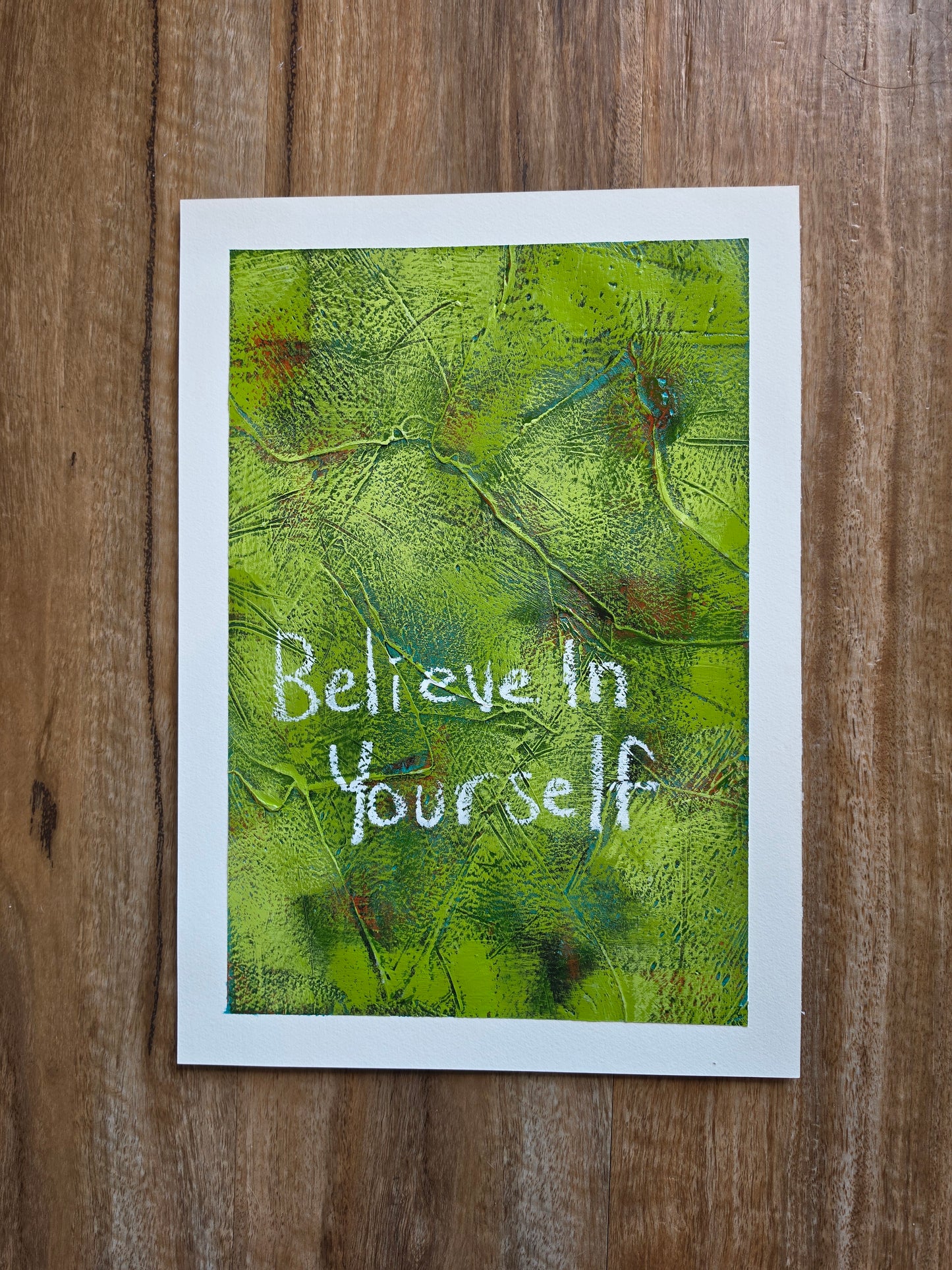 Abstract painting in green with green and red pops of colour in underneath layers with words Believe in yourself in white handwriting with alot of texture