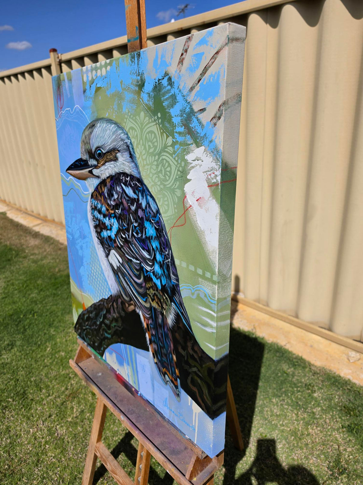Side-angle view of “Liberation,” an original mixed media oil painting of a kookaburra by Australian artist Hanna Edwards, displayed outdoors on an easel, showing the textured gallery-wrapped canvas and painted edges.