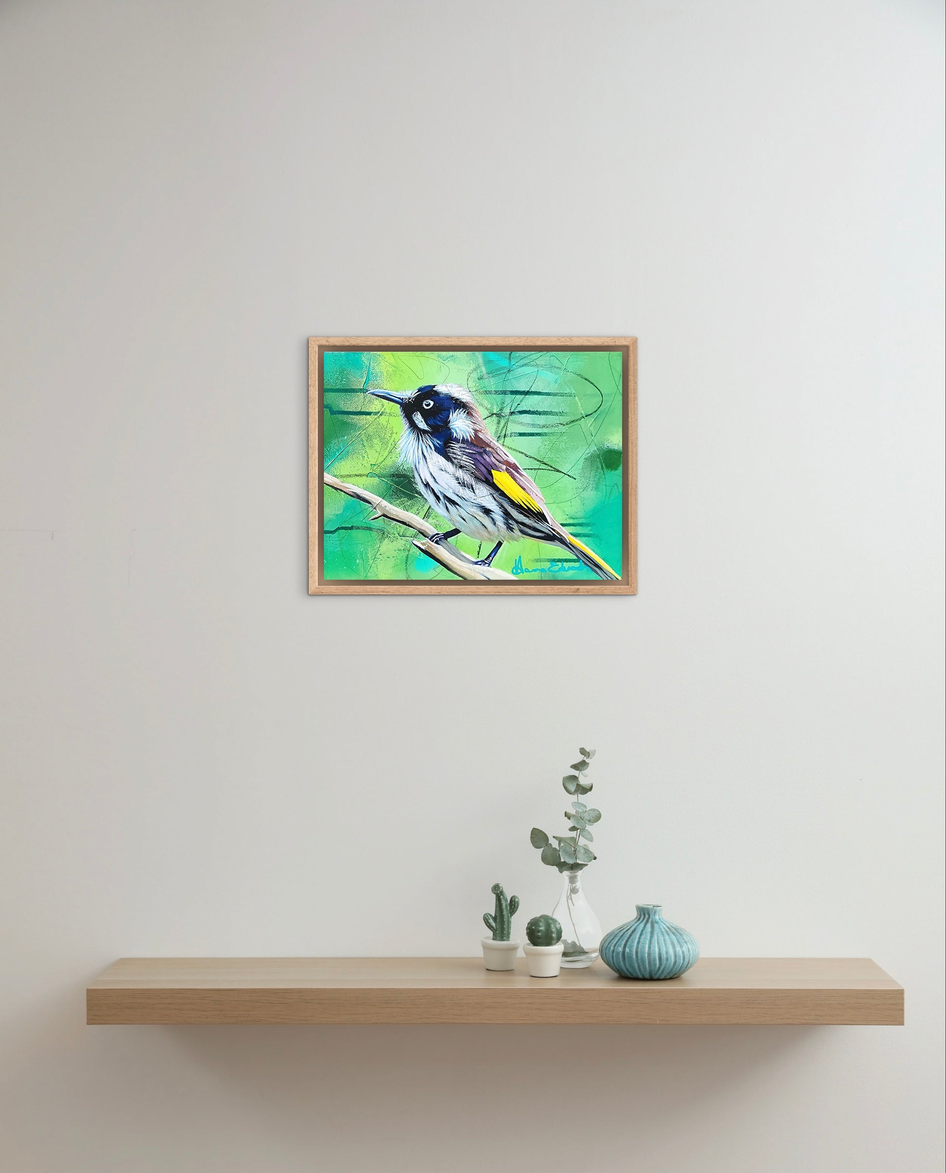 Framed artwork of a bird on a white wall above a wooden shelf with decorative items.