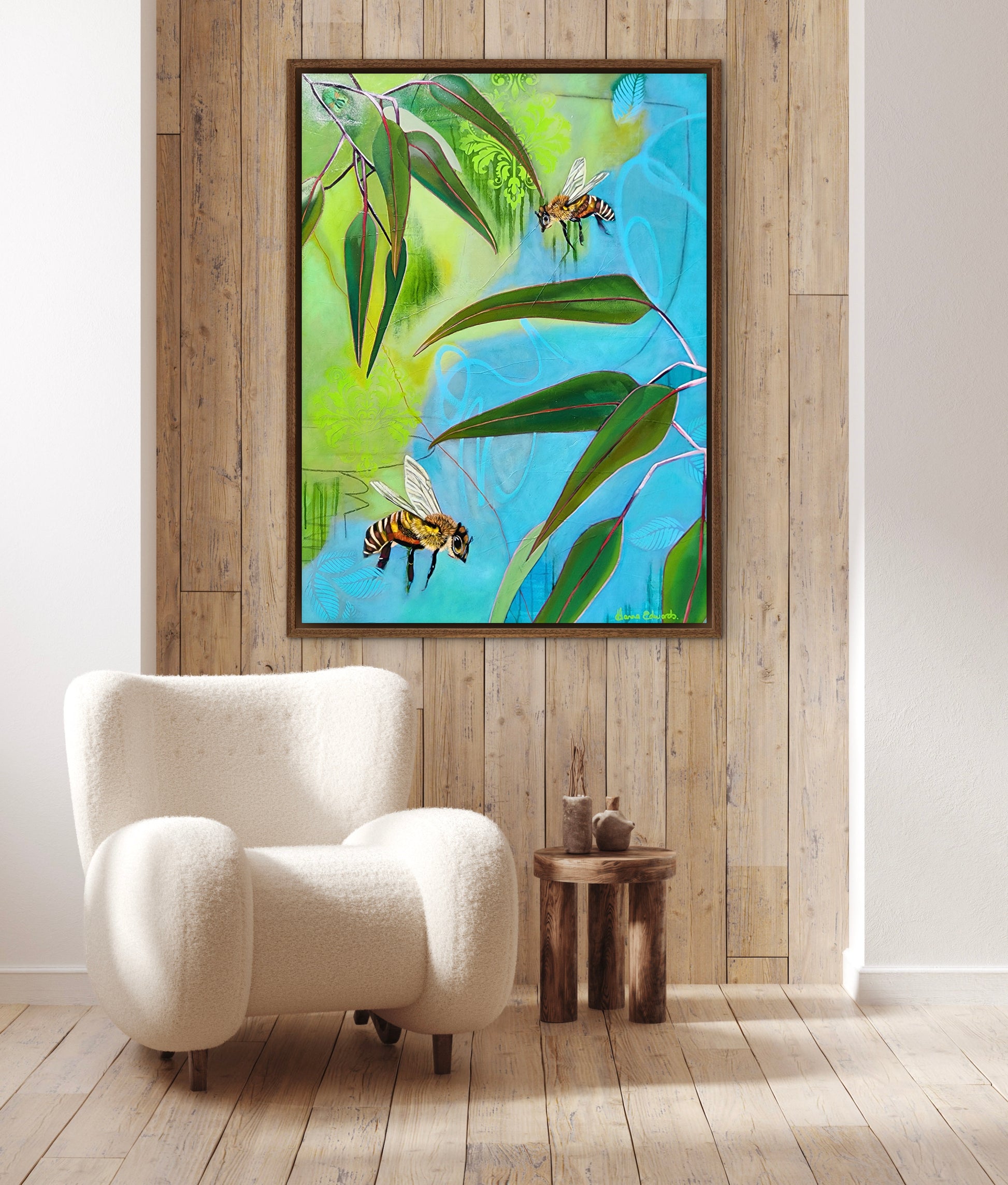 Framed artwork of bees and leaves on a wooden wall above a white armchair.