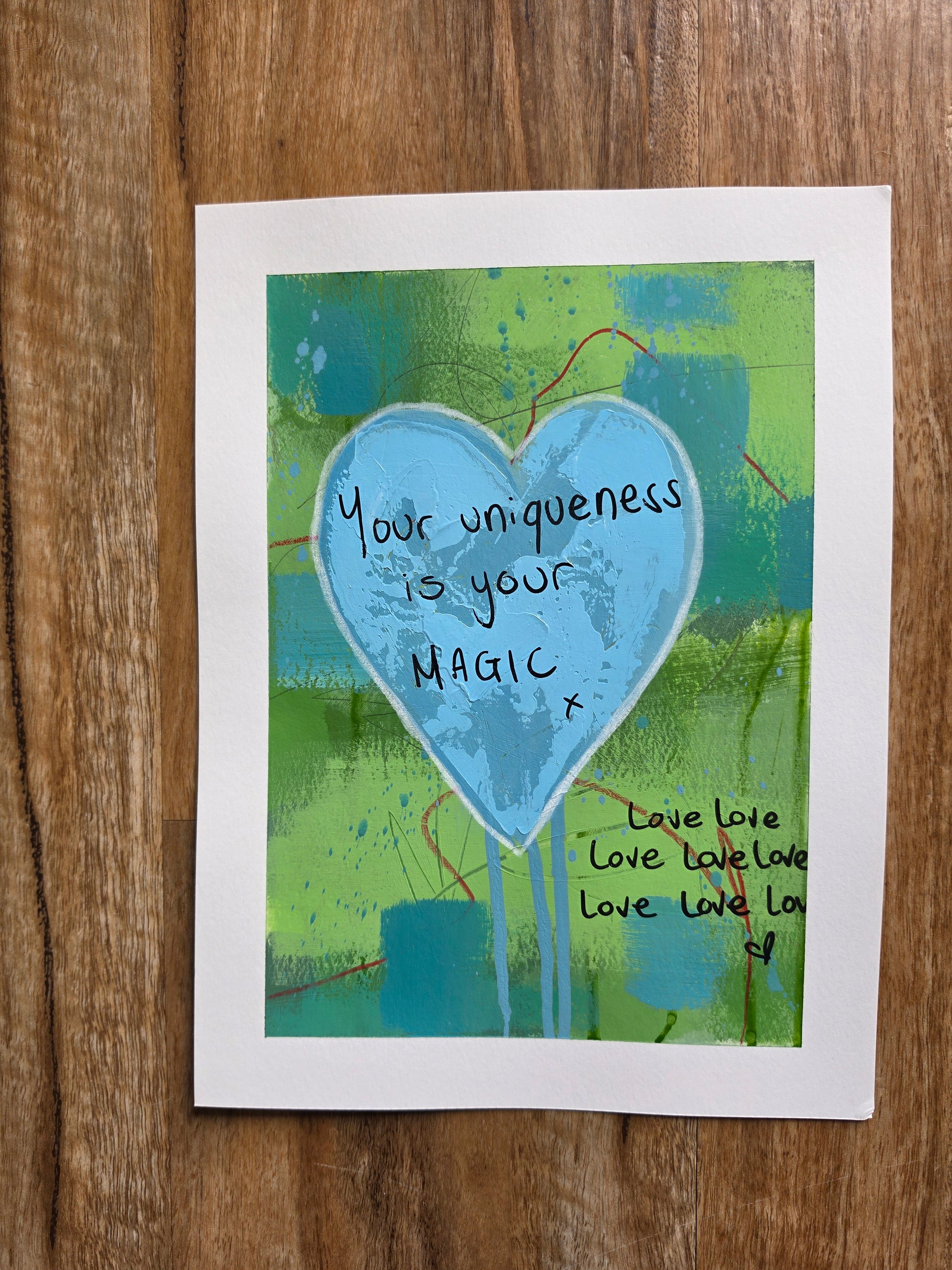 Abstract painting with a blue heart and text your uniqueness is your magic on a wooden surface