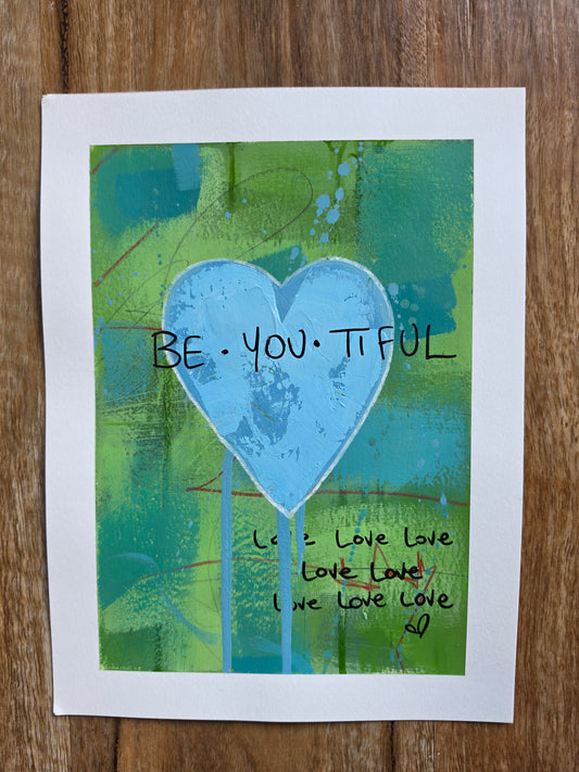 Abstract artwork with a blue heart and 'BE YOU TIFUL' text on a wooden surface