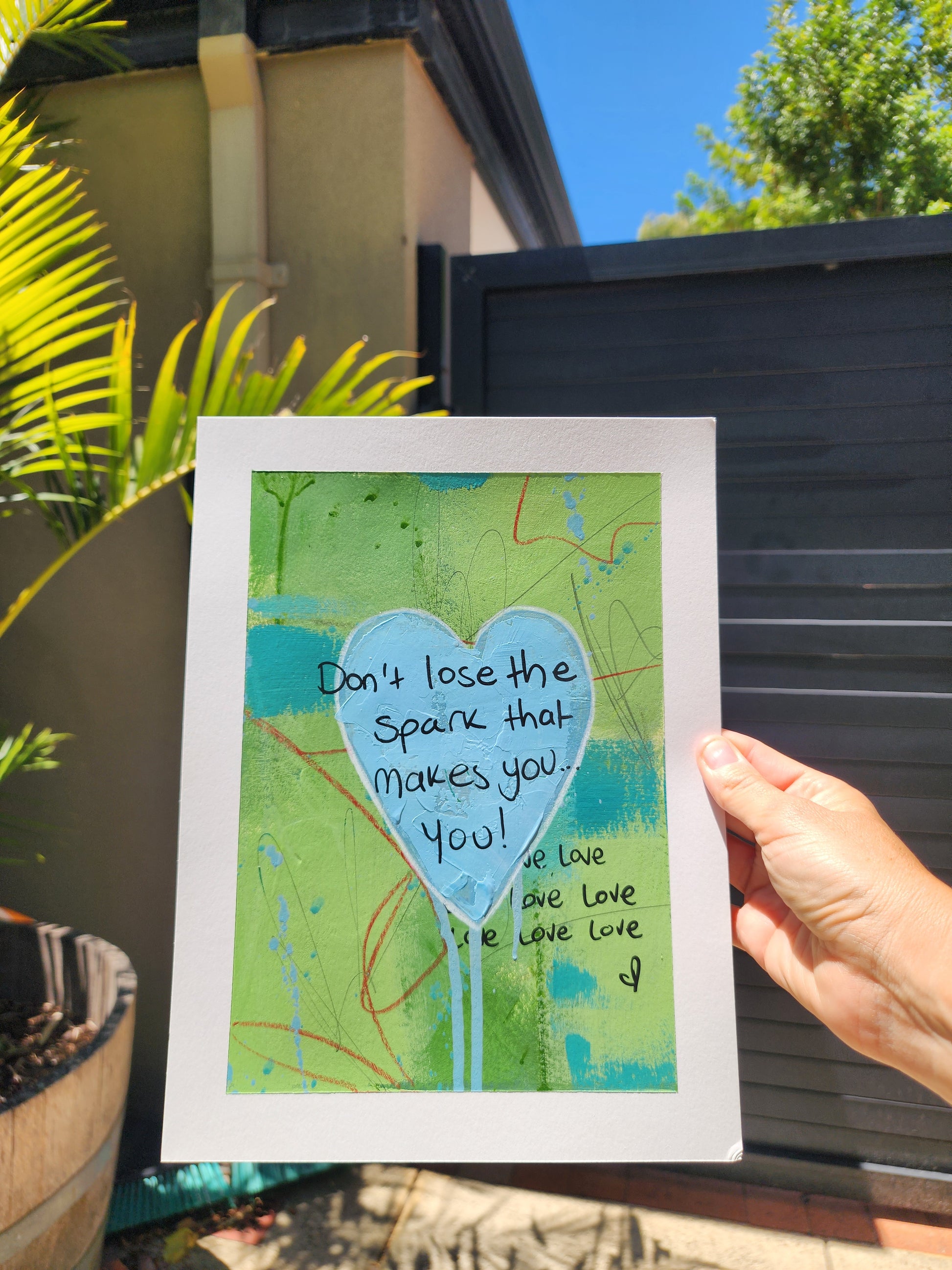 abstract artwork with a heart and text, held outdoors.