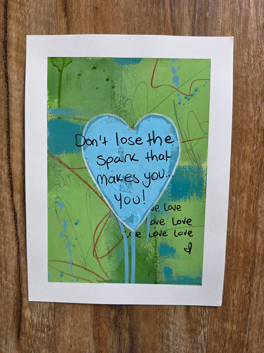 Abstract artwork with a blue textured heart and text on a green background, placed on a wooden surface.