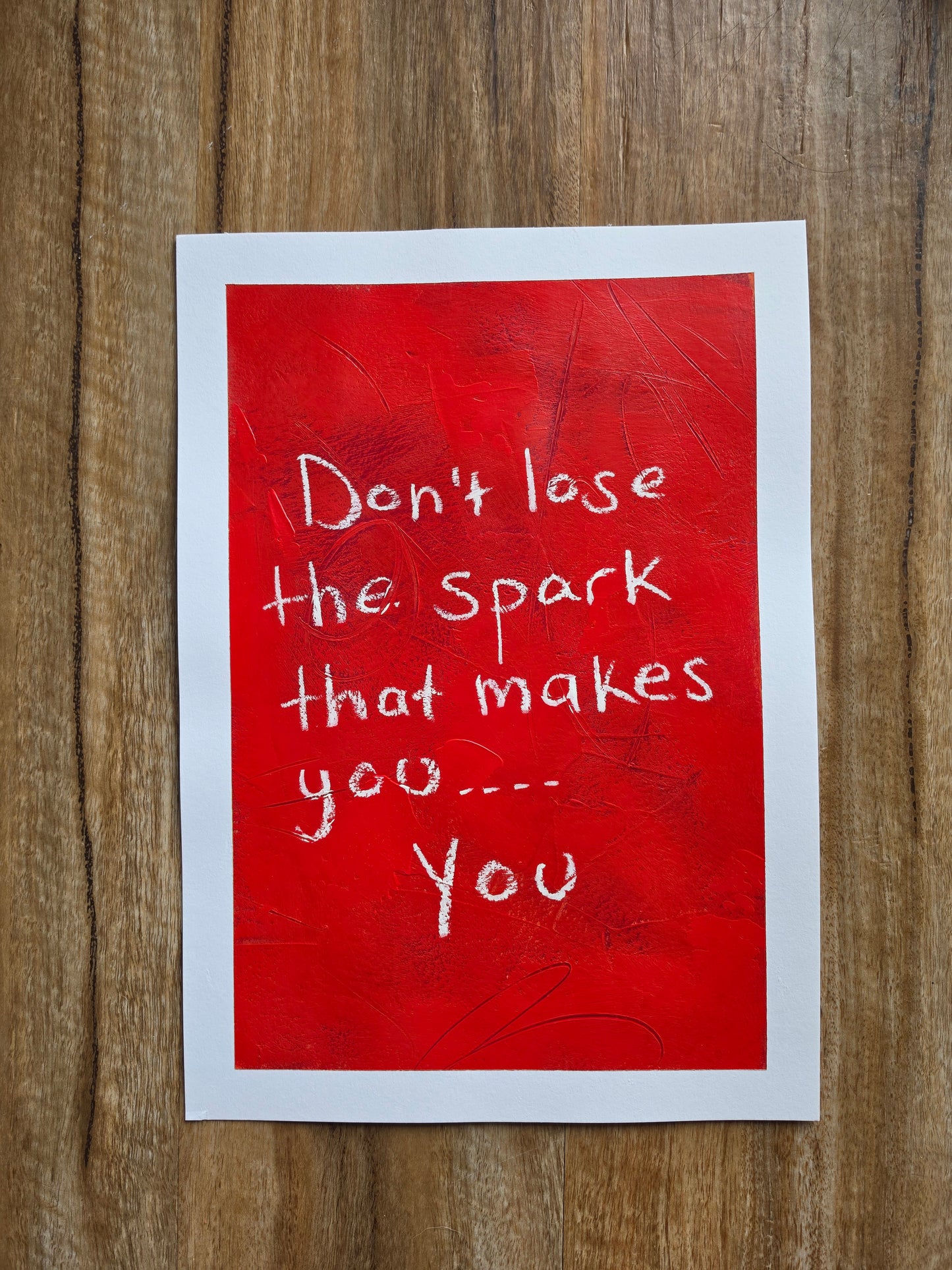 Red painting white text  Don't lose the spark that makes you.. you, on a wooden surface