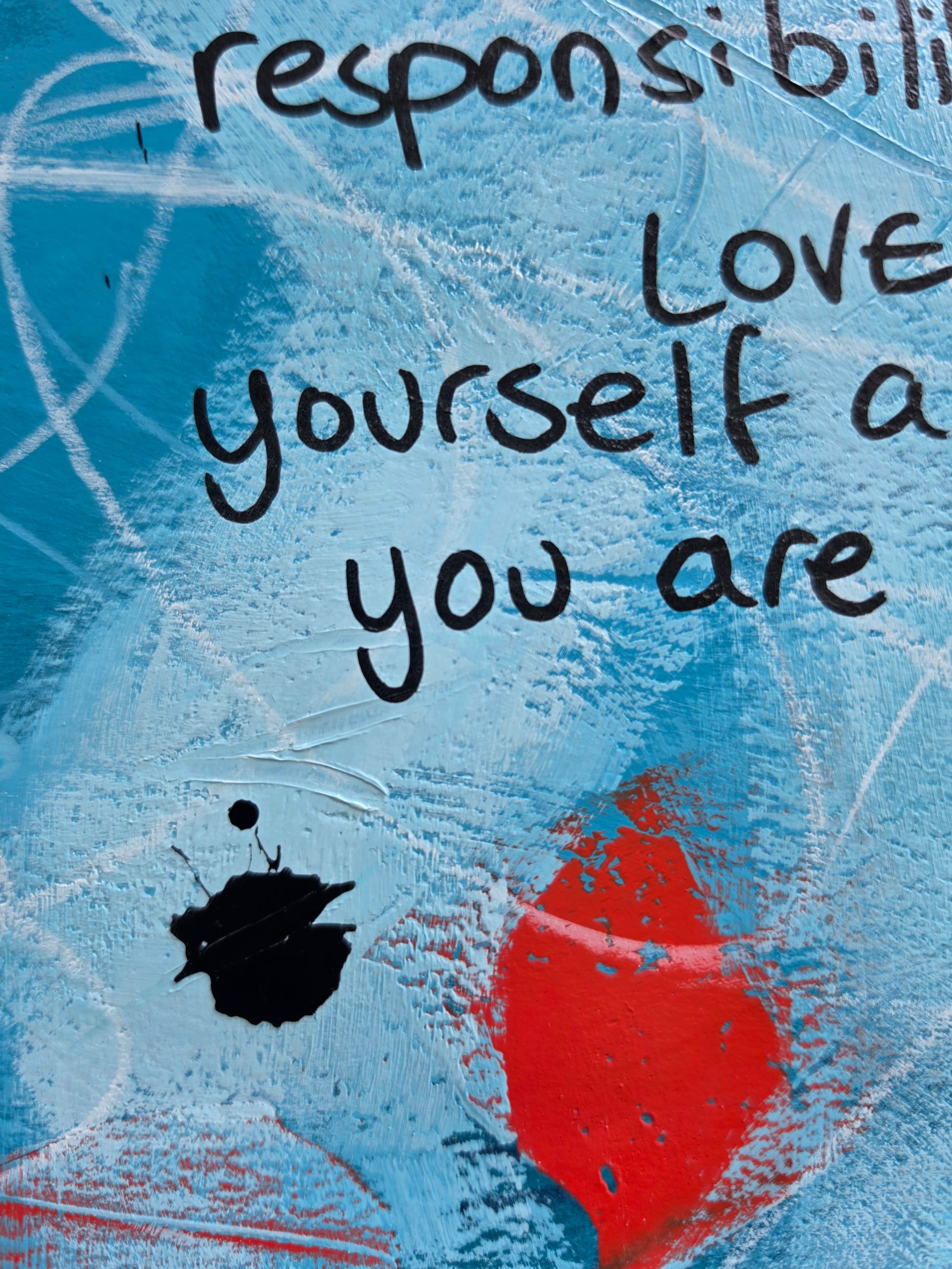 Abstract painting in blue with scribble marks, black drips and pops of bright red with the words in black handwriting