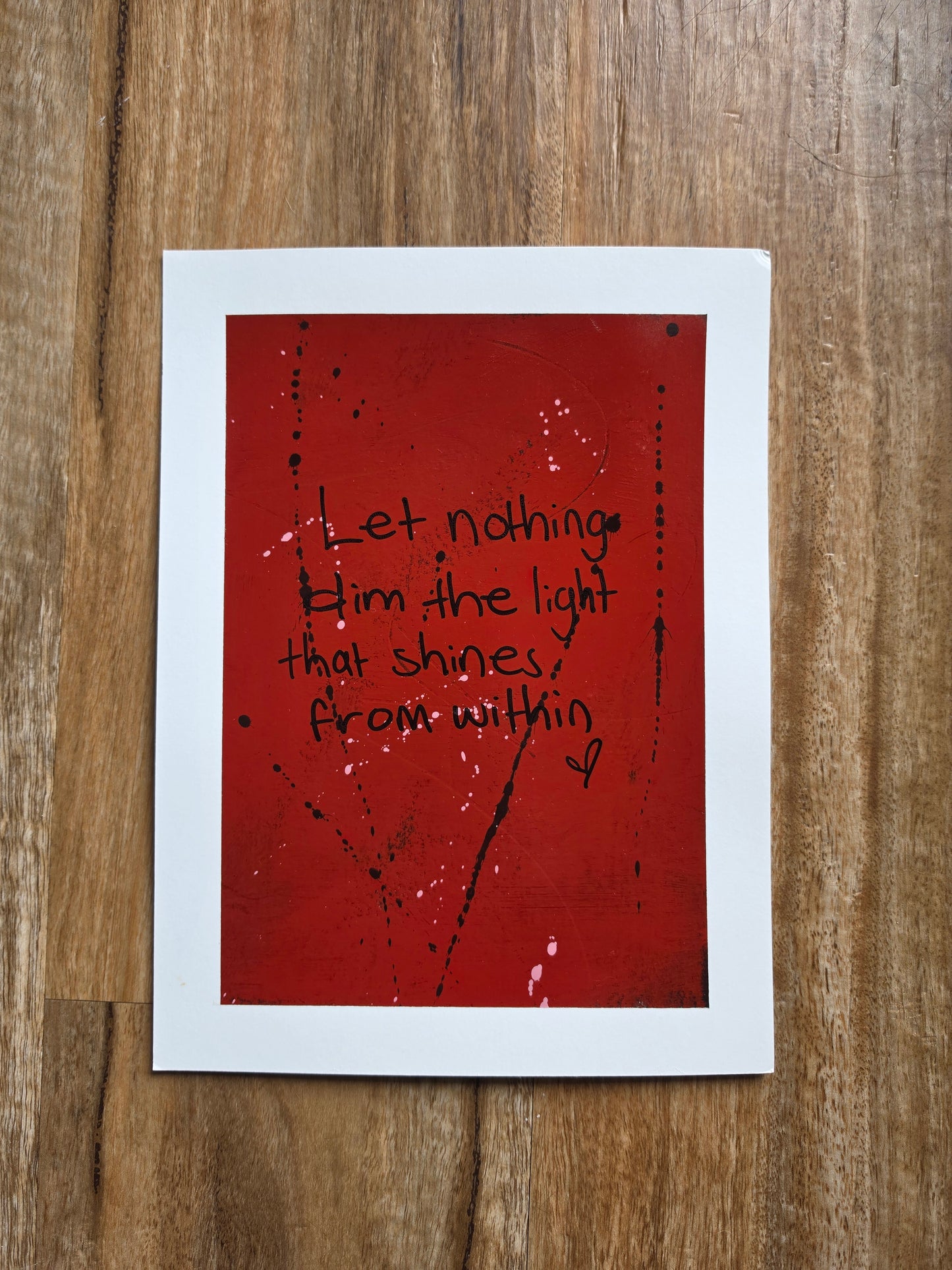 Red painting with the words let nothing dim the light that shines from within in black text on a wooden surface