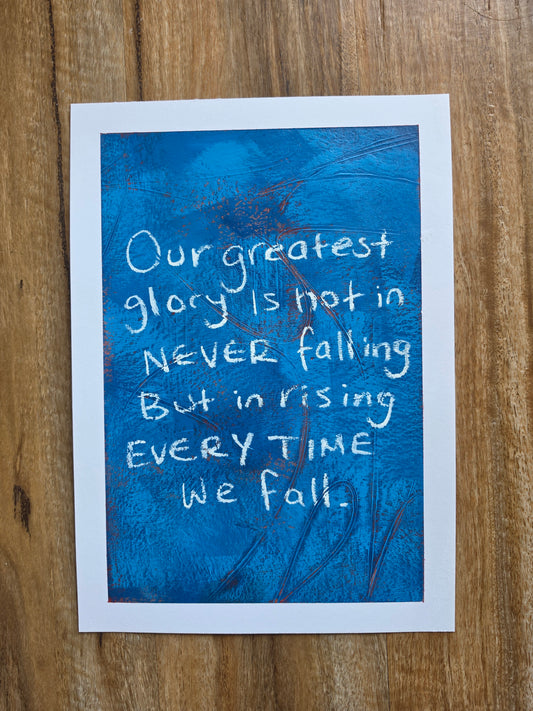 Blue painting with pops of red with white text "Our greatest glory lies not in never falling but rising everytime we fall " on a wooden surface