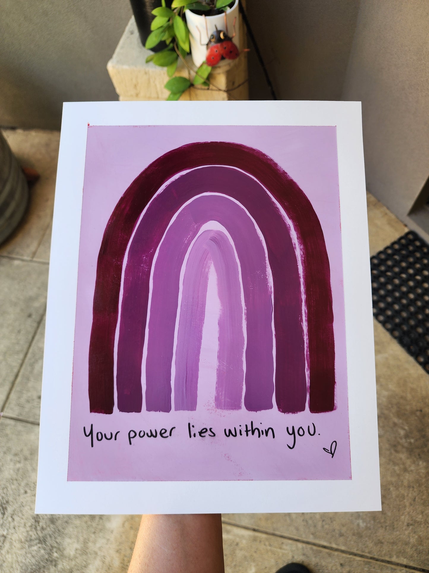 Painting with a purple monochromatic  rainbow and motivational quote your power liew within you on a light purple background, held by a person.