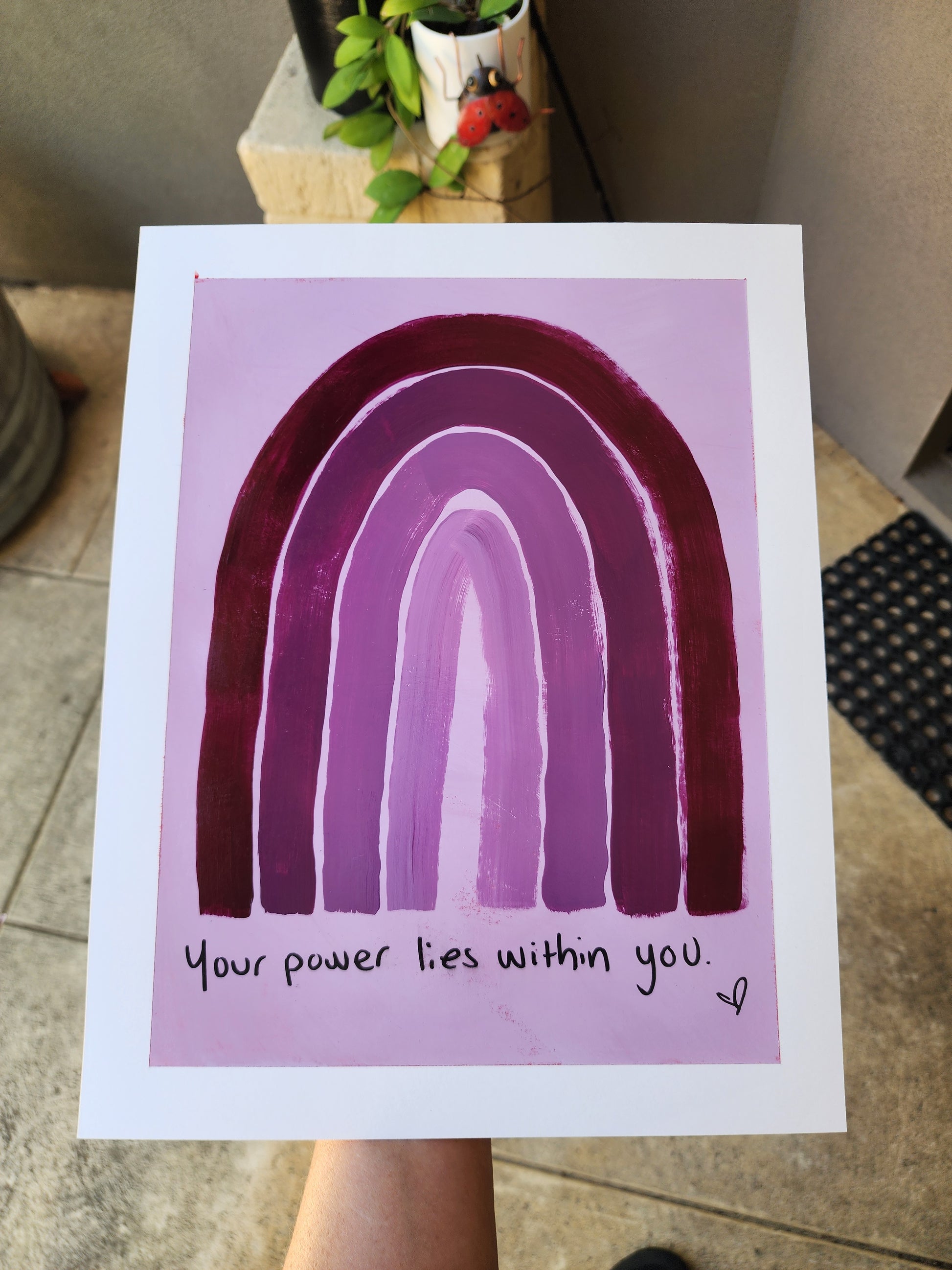 Painting with a purple monochromatic  rainbow and motivational quote your power liew within you on a light purple background, held by a person.