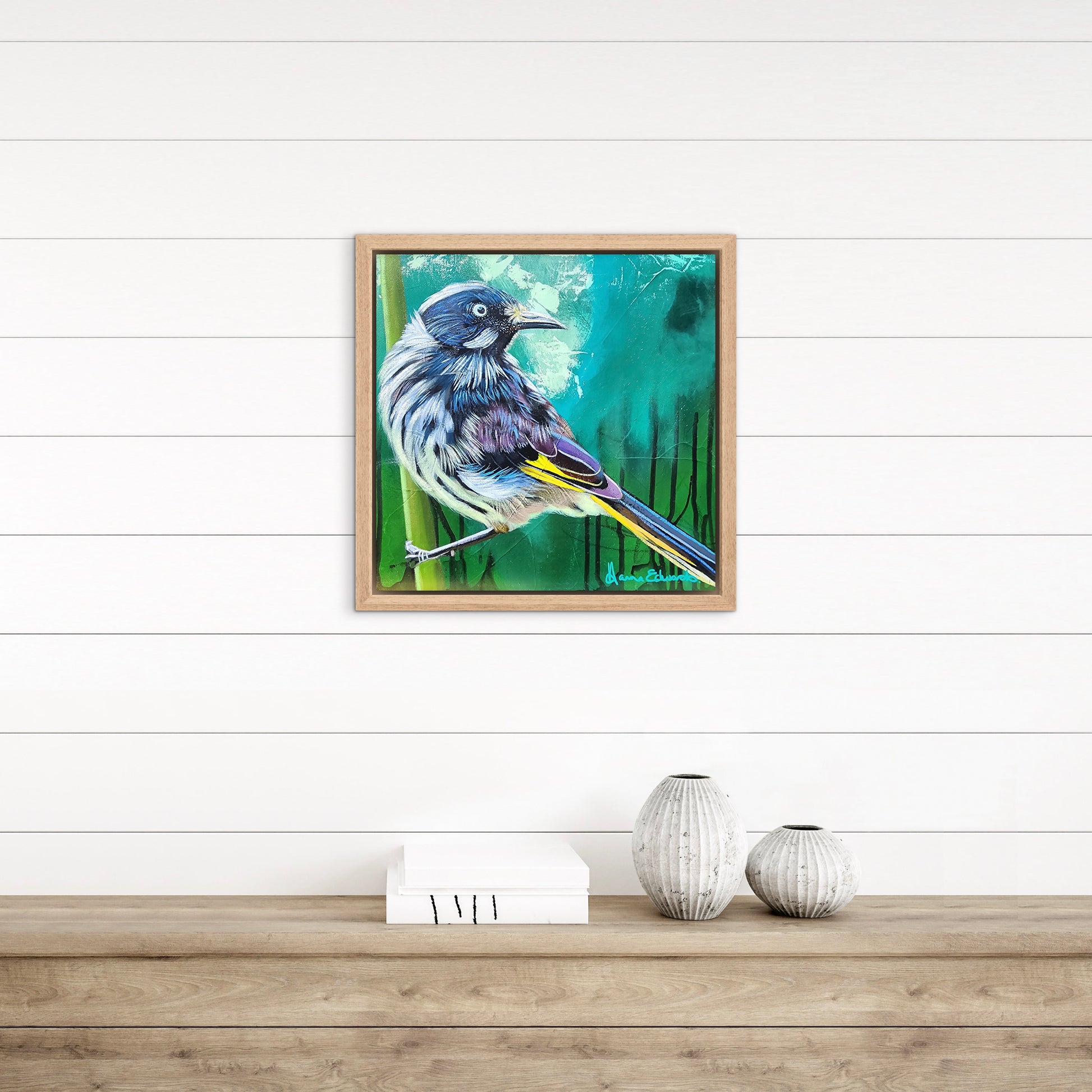 Framed artwork of a bird on a white wall with wooden shelf and decorative items.