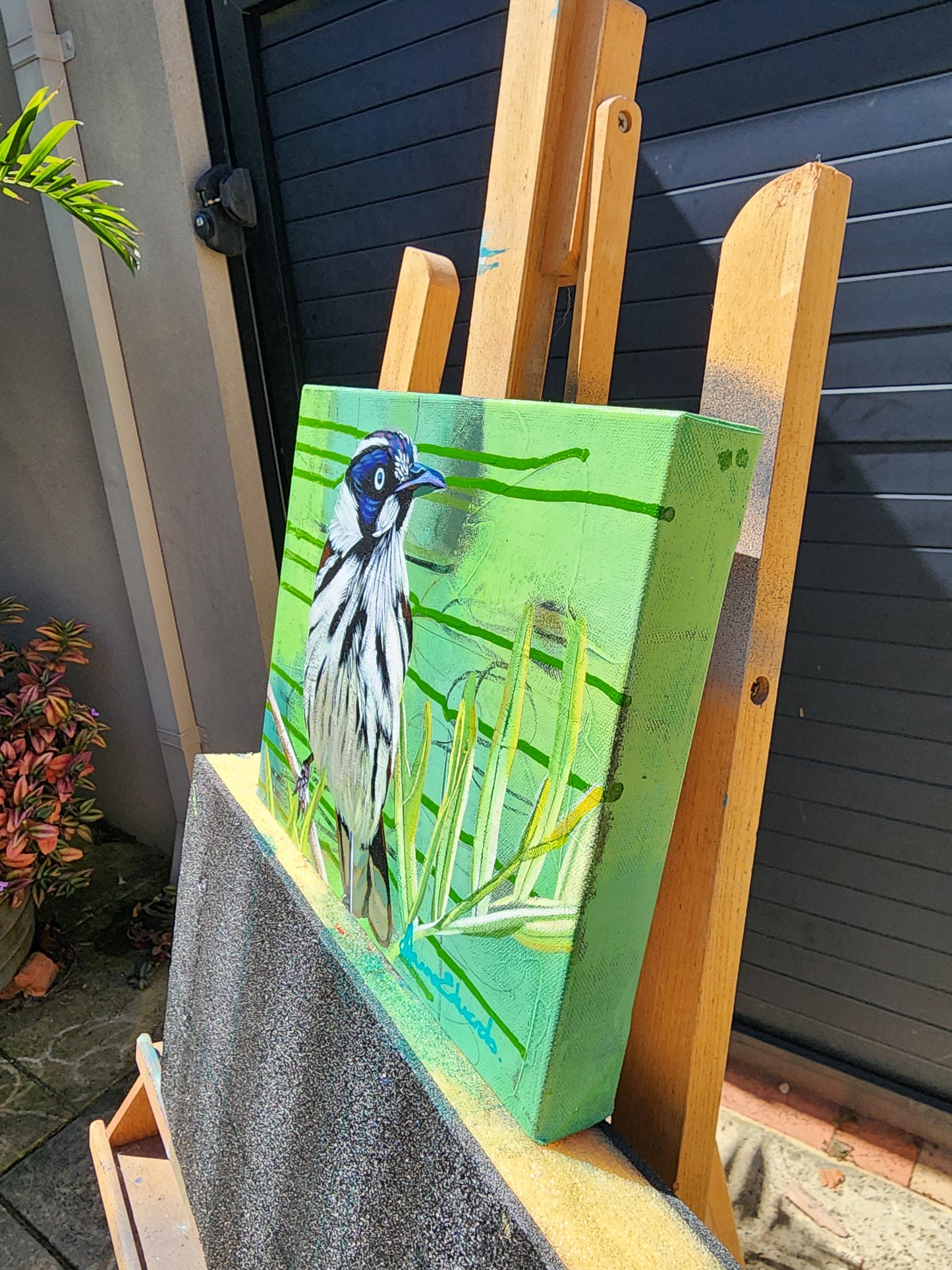 Painting of a bird on a green background held by a wooden easle