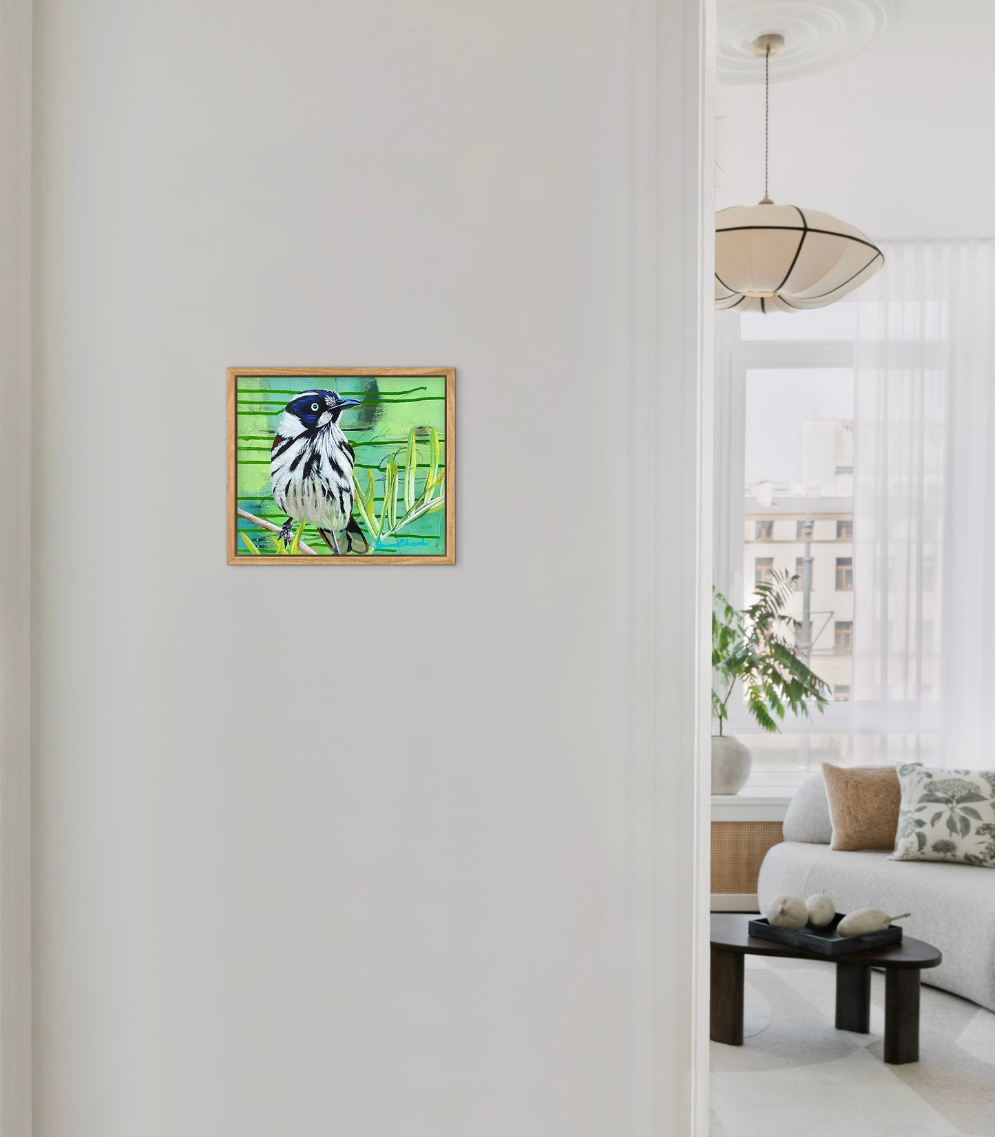 Framed artwork of a bird on a white wall with a living room in the background