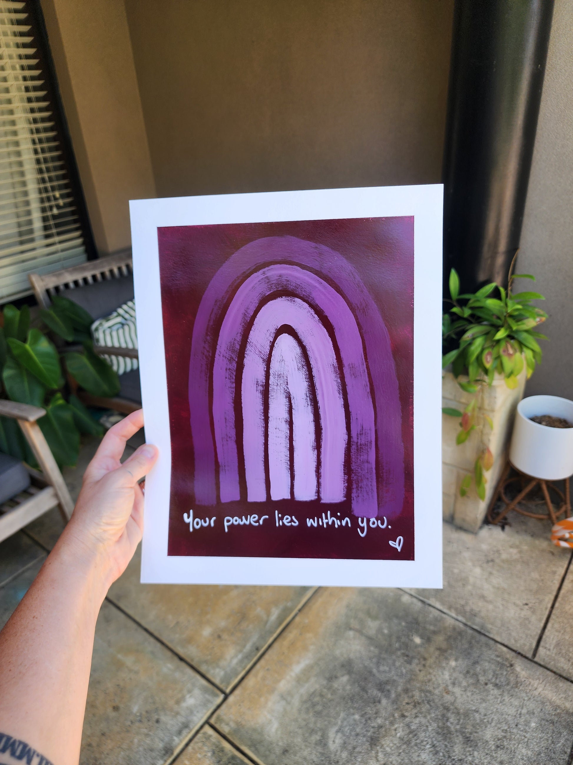 Person holding a original paper artwork of monochromatic rainbow with quote your power lies within you  on purplered background
