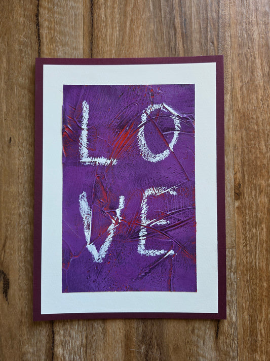 Heavily textured painting in purple with pops of red coming through with the word Love white boarder glued to a red violet matt board