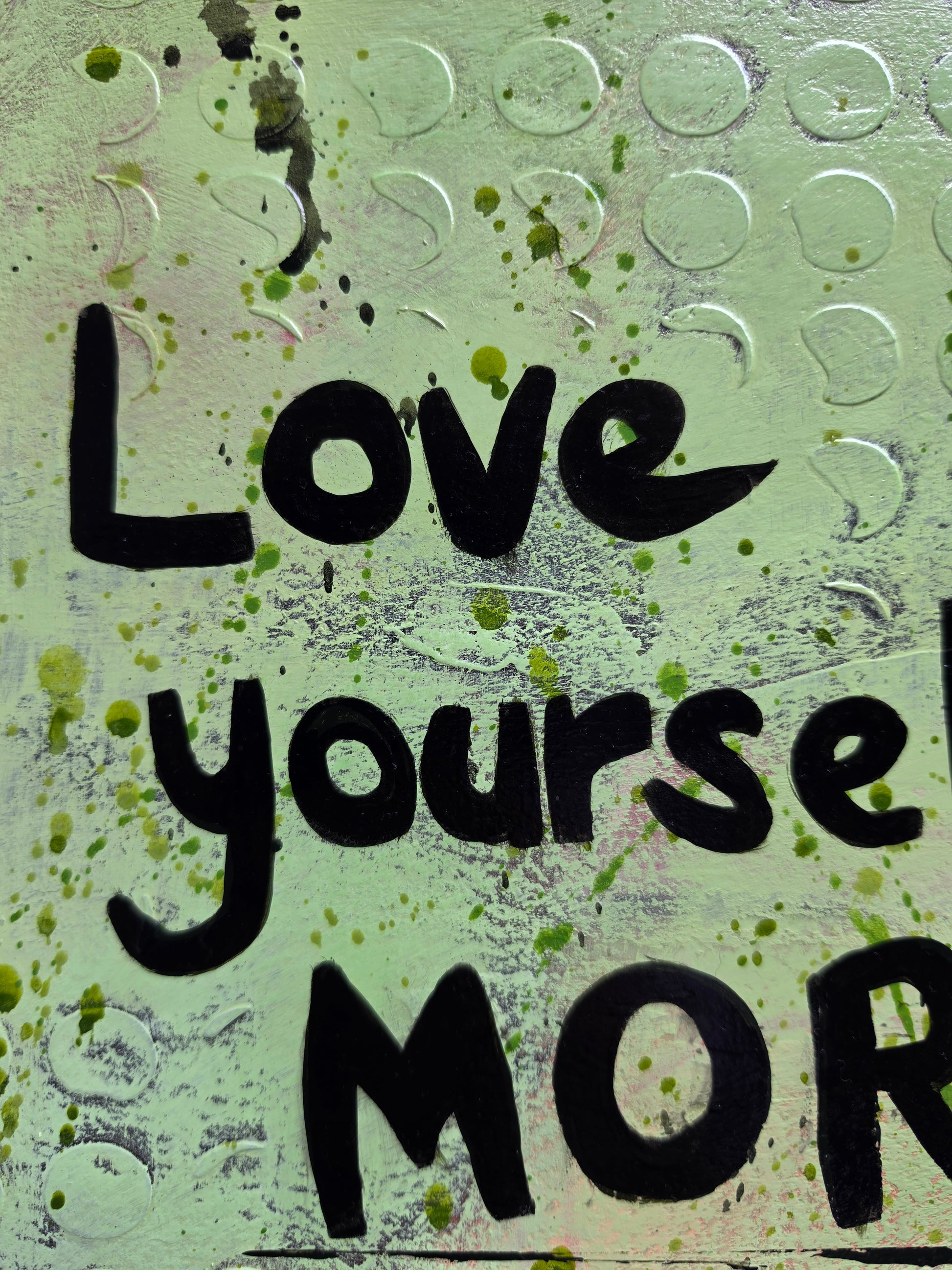 Close-up of a textured light green surface with black hand-lettered text reading 'Love your MOR' and scattered green paint splatters.