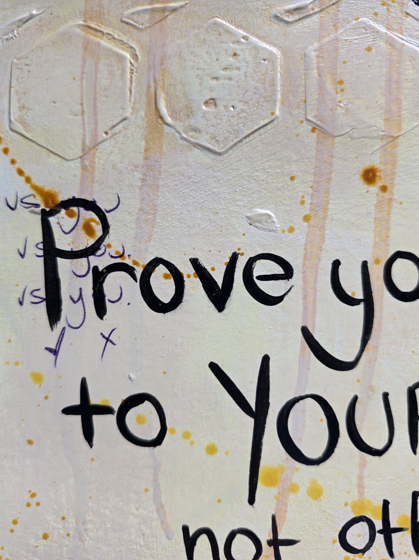 A close-up of a textured yellow surface with embossed hexagonal patterns, handwritten black text reading 'Prove it to yourself', and small yellow-orange paint splatters.