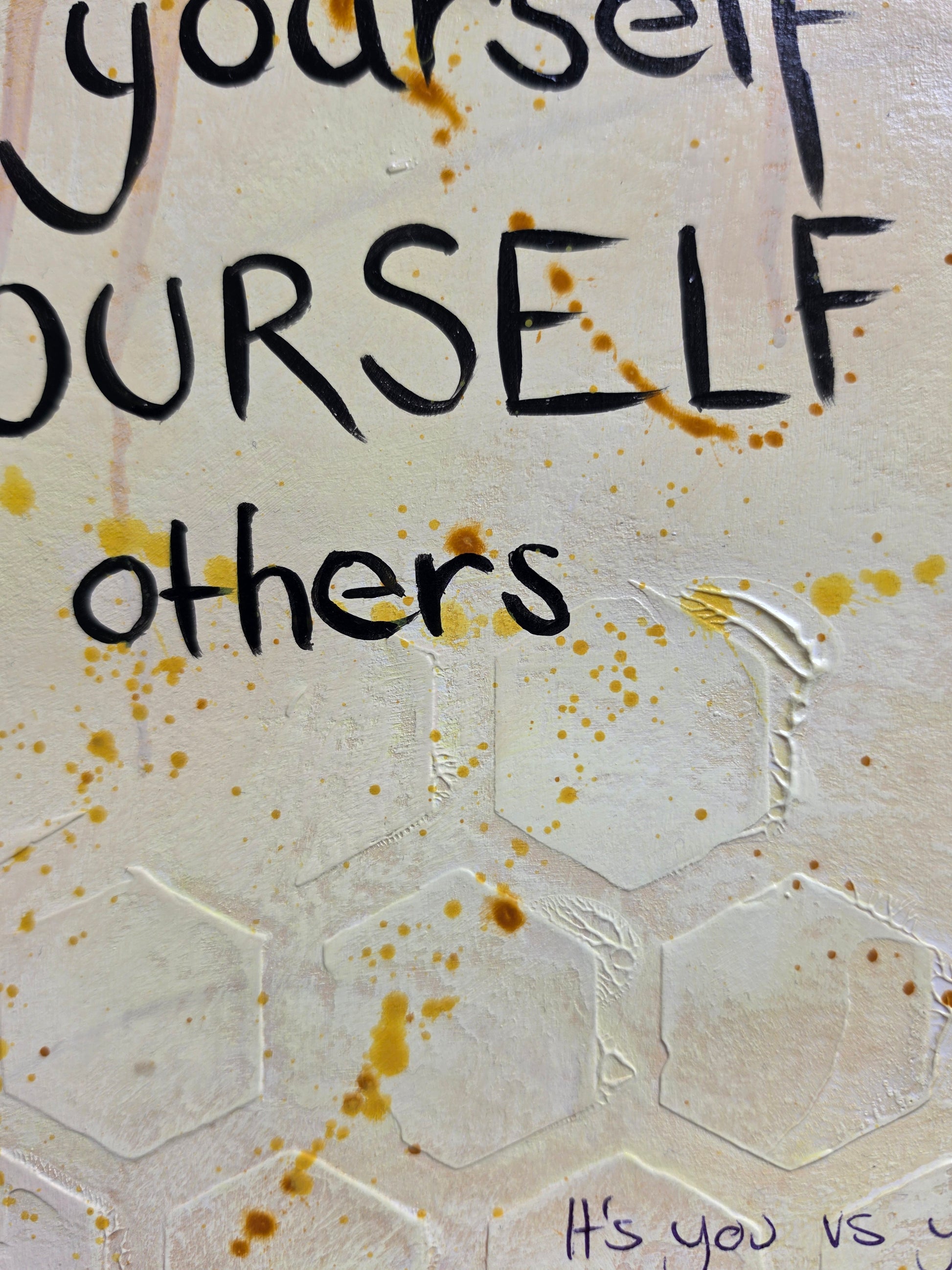 A close-up of a textured cream-colored painting on paper  featuring embossed hexagonal patterns, hand-lettered black text, and warm brown paint splatters.