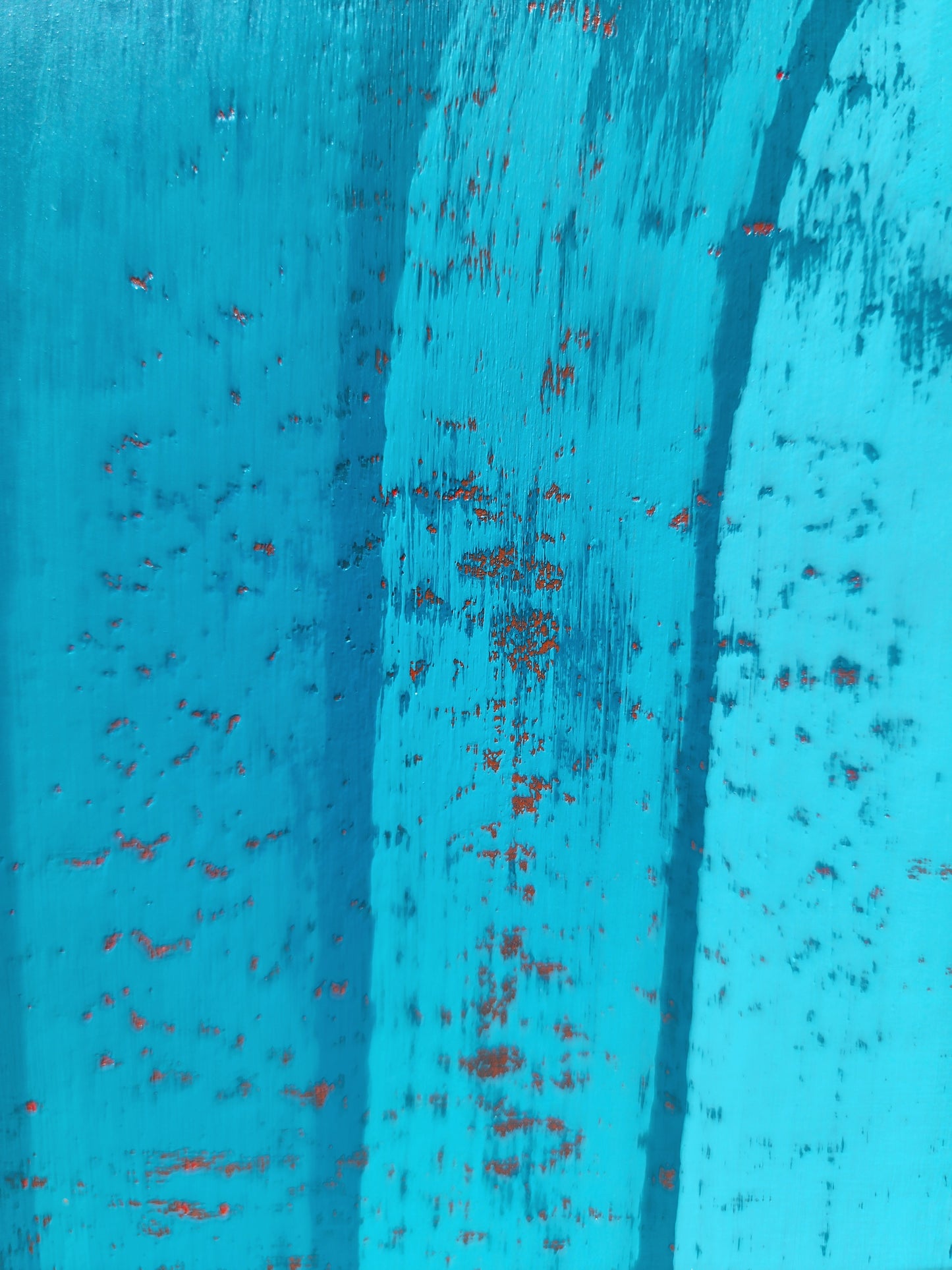 A close-up of a textured turquoise blue painted surface with distressed vertical streaks that form the arch with small red speckles showing through