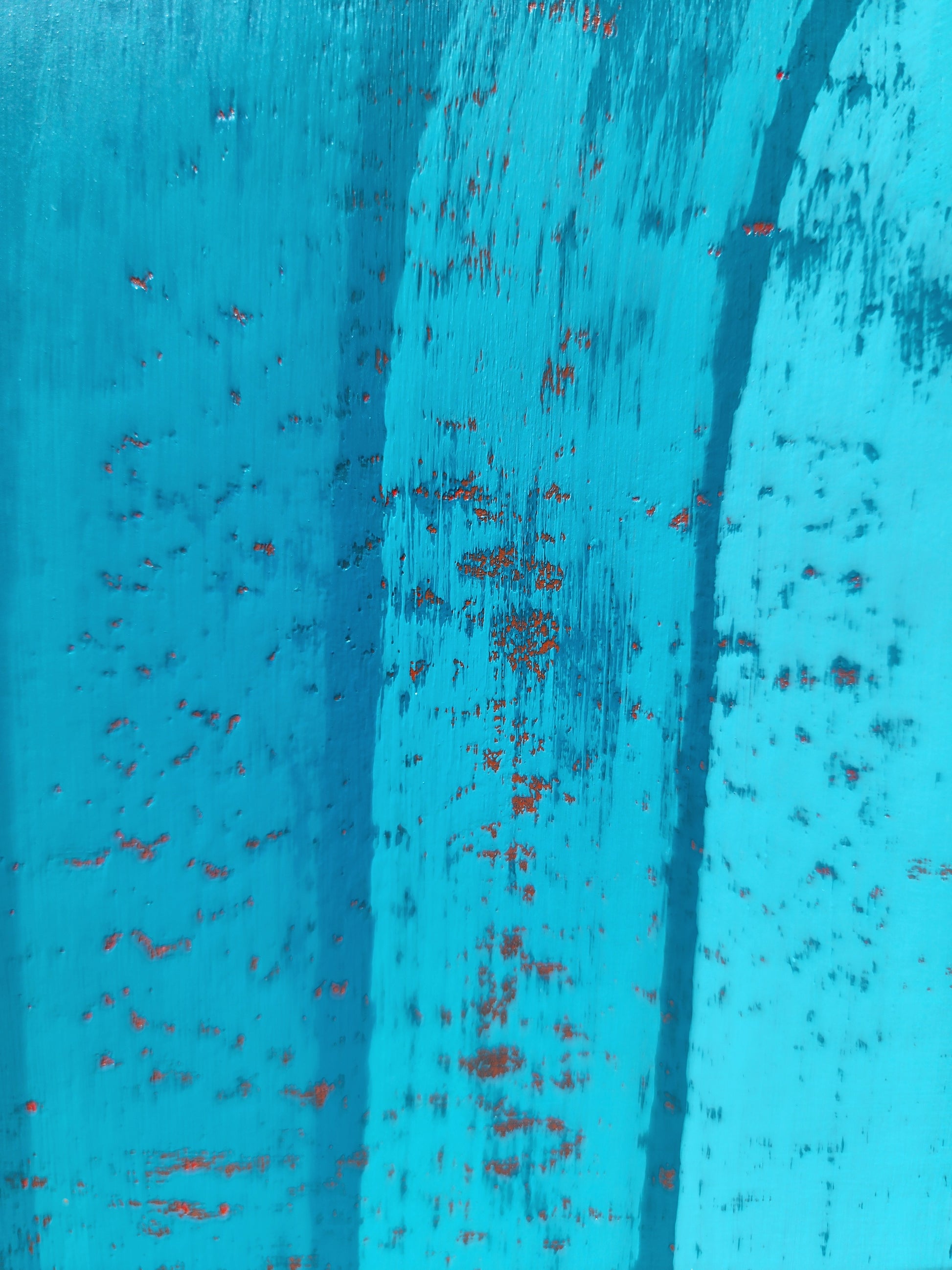 A close-up of a textured turquoise blue painted surface with distressed vertical streaks that form the arch with small red speckles showing through