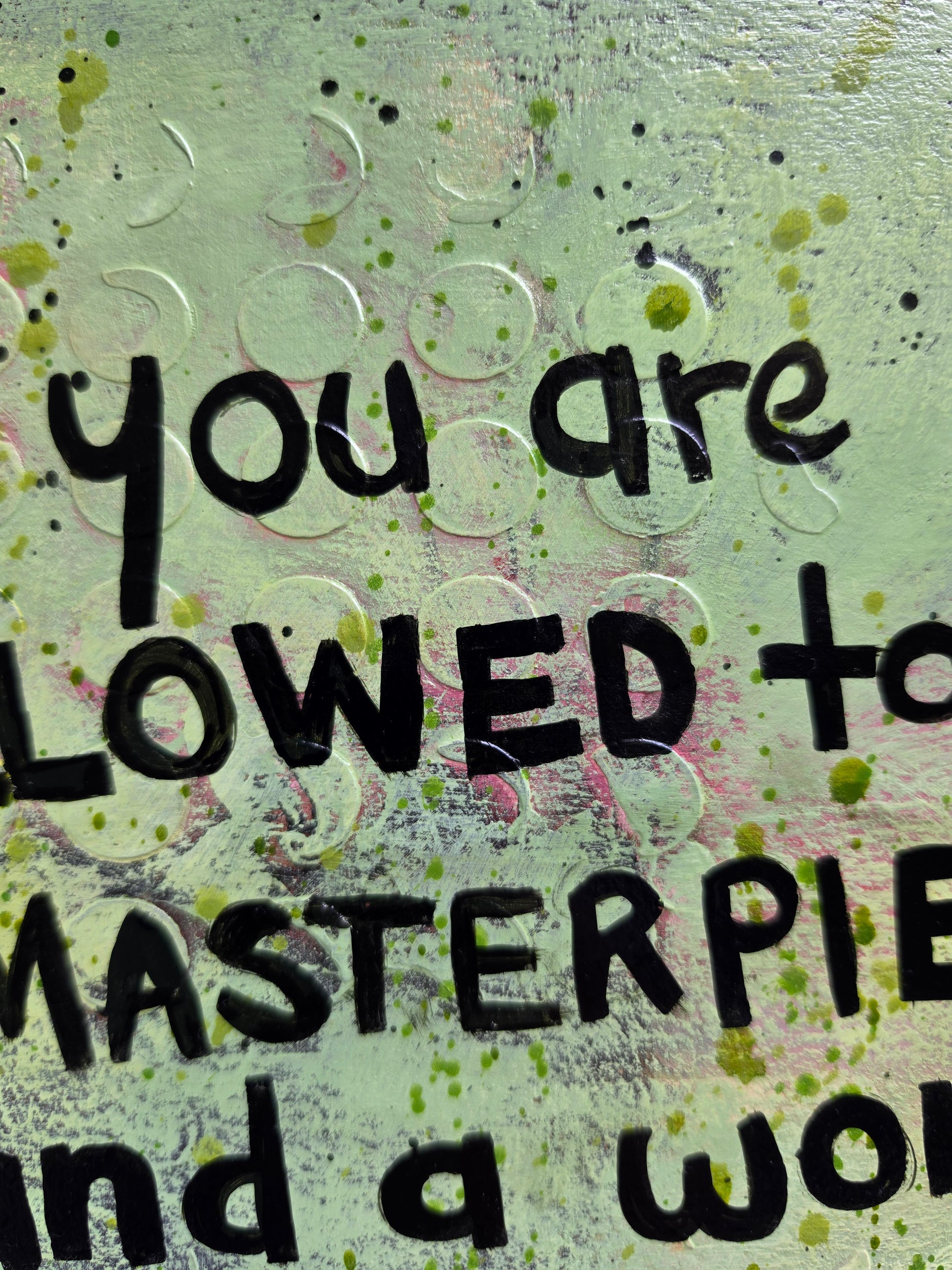 Close-up of a textured background featuring black hand-lettered text on a distressed light green background with paint splatters and circular embossed details.
