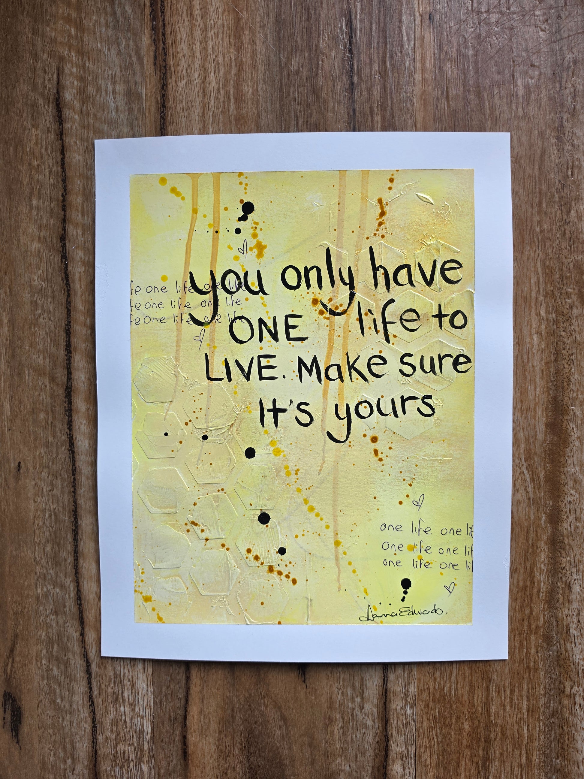 A painting with a white border featuring a yellow textured background and the hand-lettered quote 'you only have ONE life to LIVE. Make sure It's yours', displayed flat on a brown wooden surface