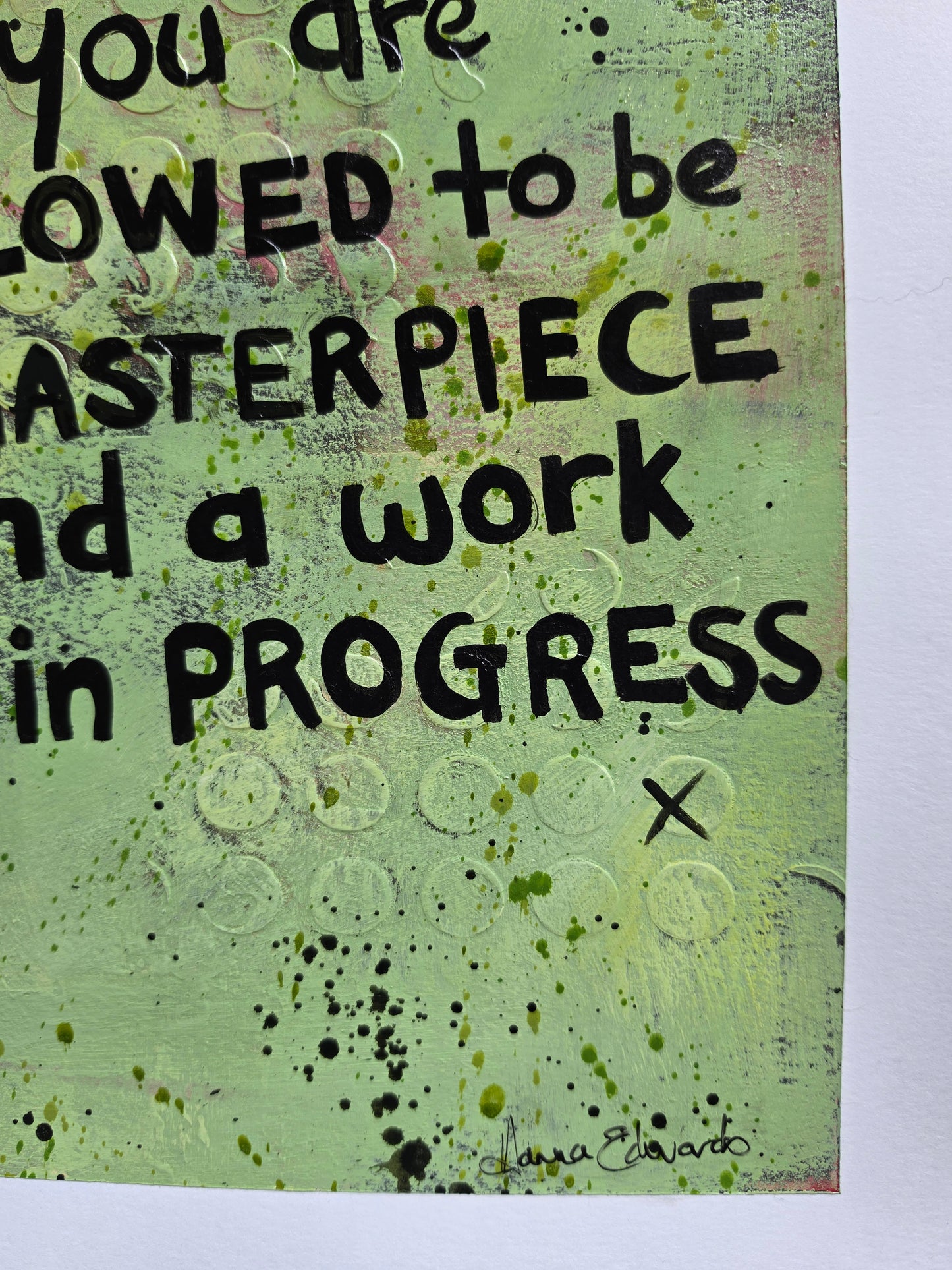 A close-up of a textured art featuring a quote in black hand-lettered text on a light green background with paint splatters and circular texture details. Artist Hanna Edwards Signature